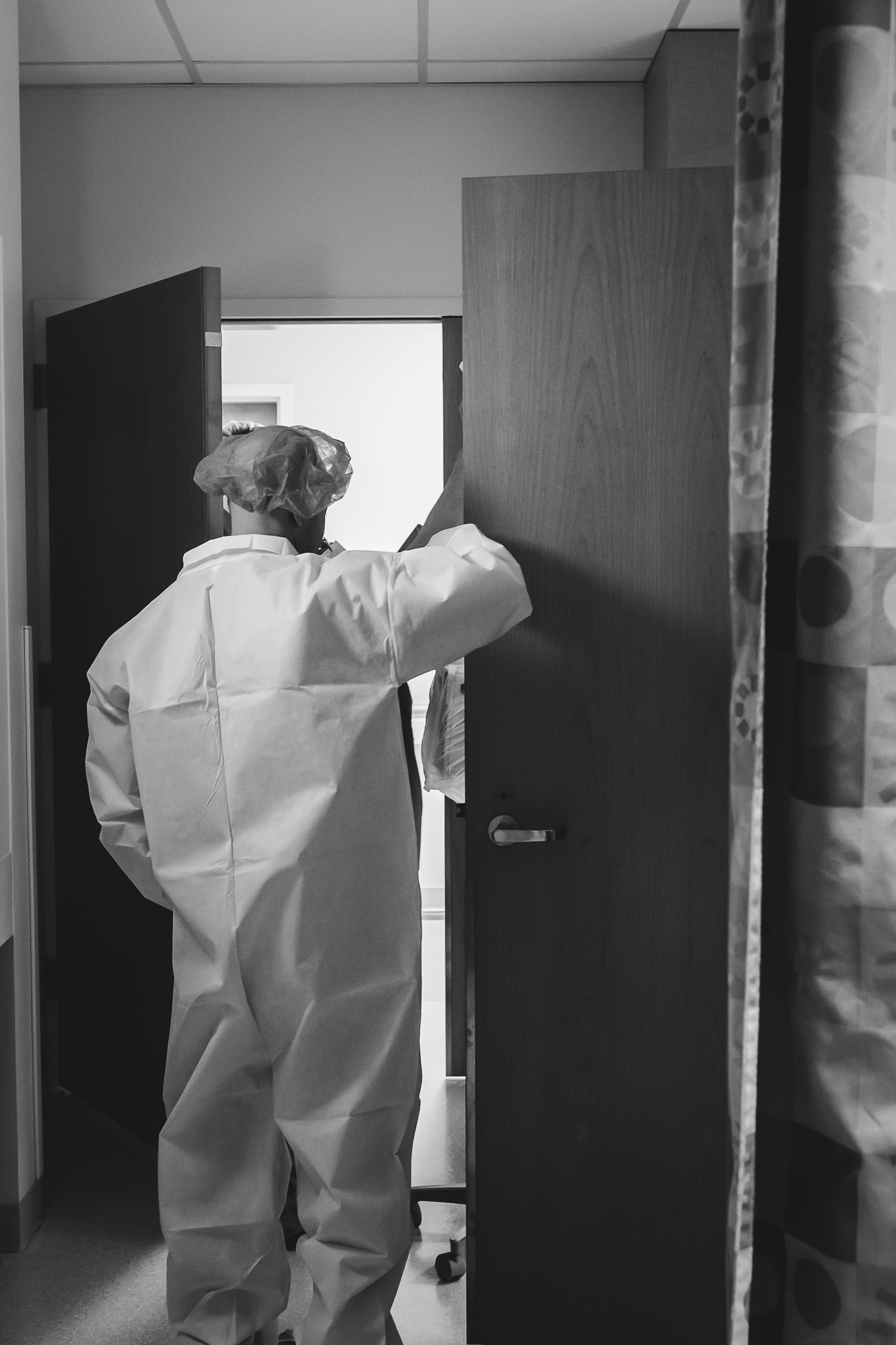 A man in surgery scrubs walks out of a hospital room. 