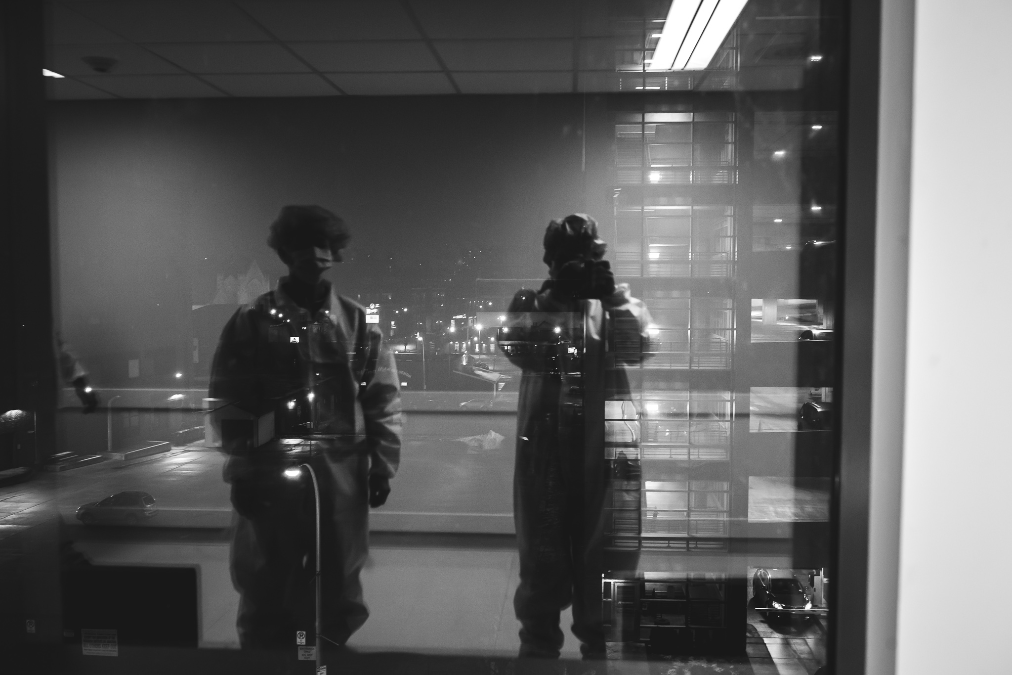 Black and white reflection of a man and photographer in a hospital window.