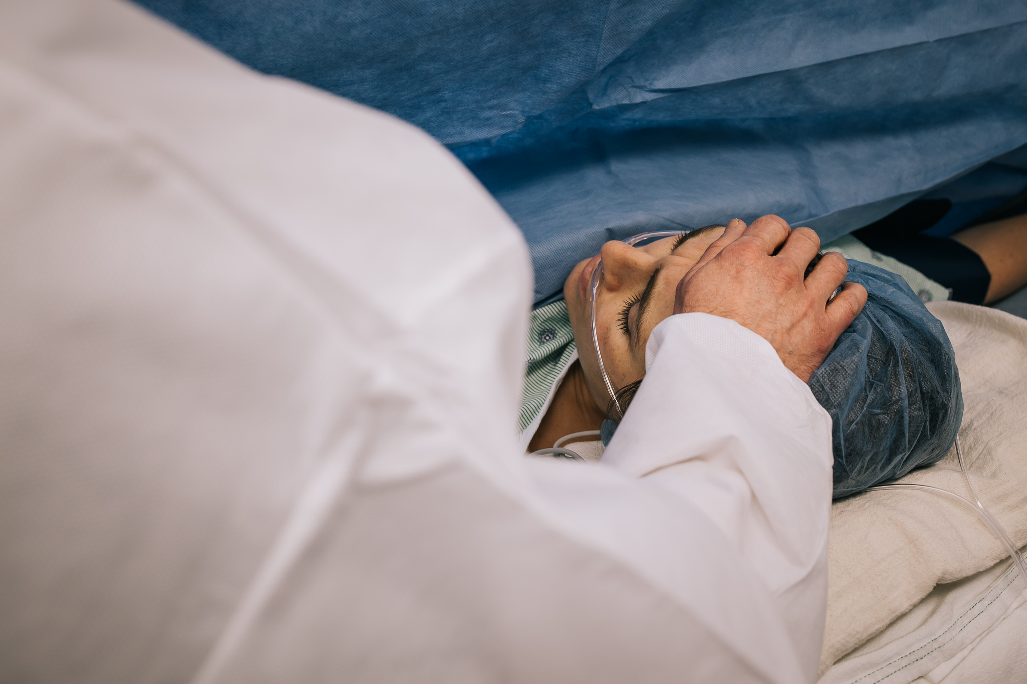 husband holds his hand on his wife's forehead during c-section.