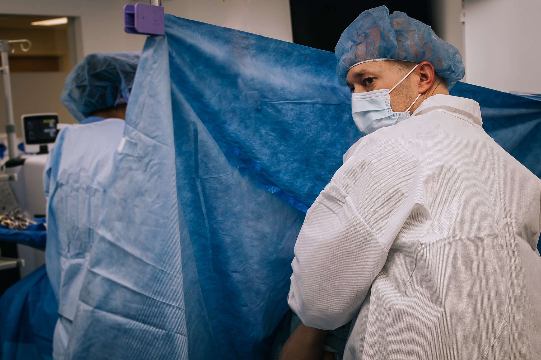 A dad looks over his shoulder at his newborn baby in the warmer.