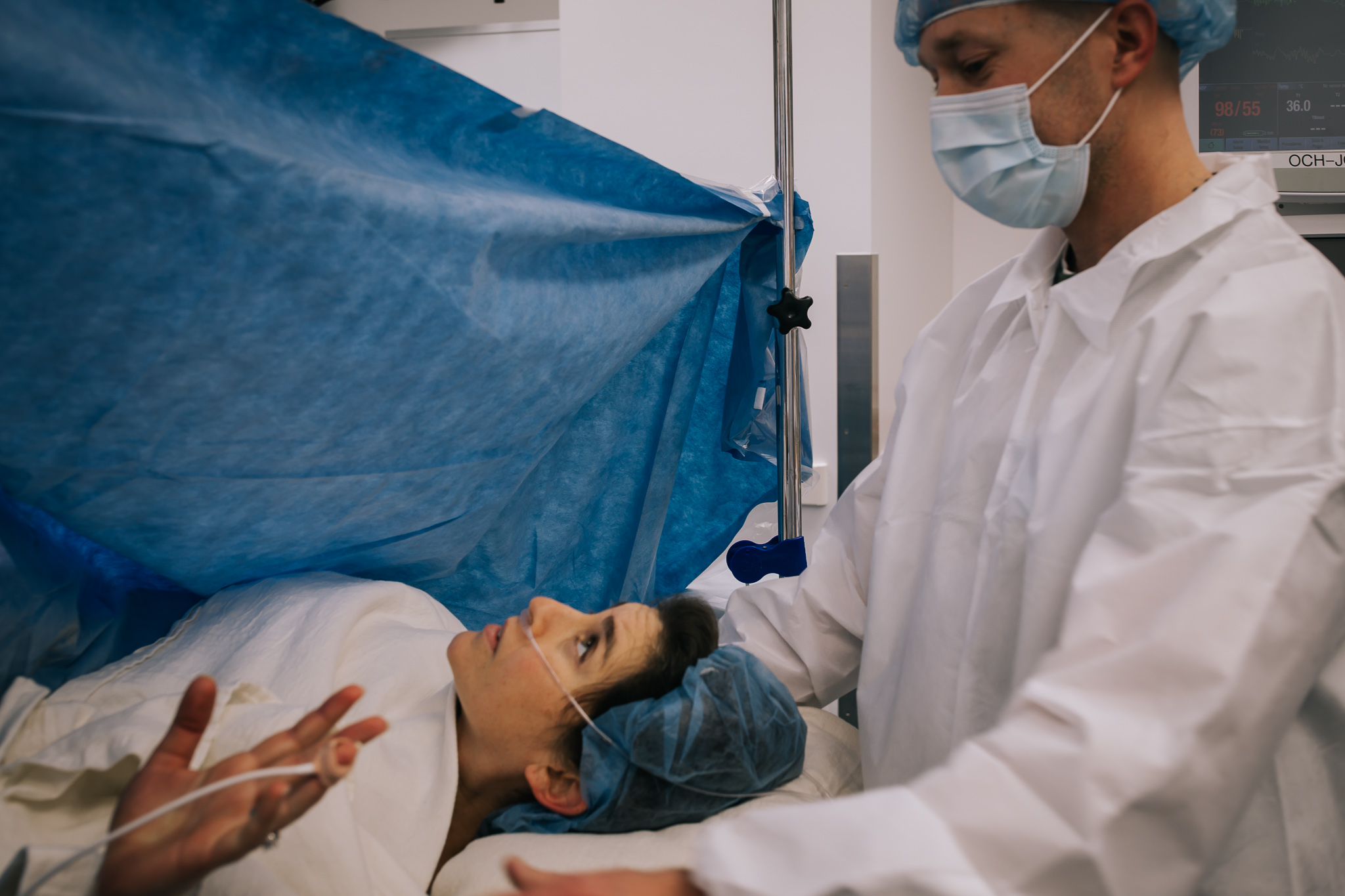 A woman reaching for her husband's hand during a cesarean section surgery.