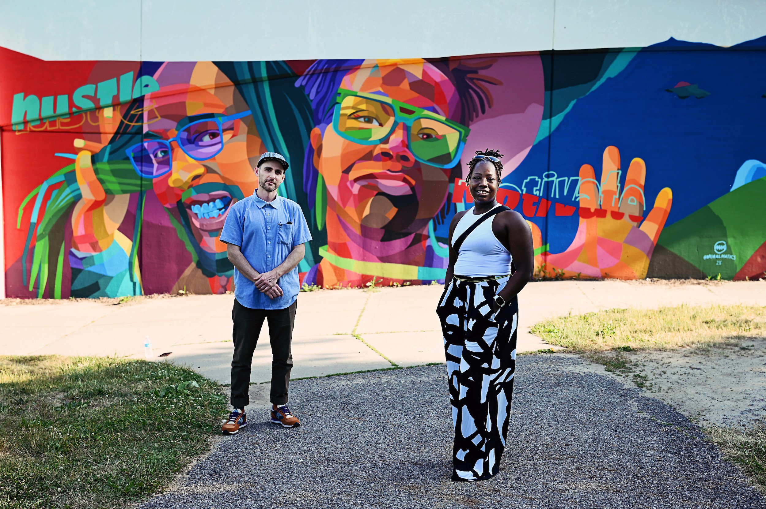  Muralmatics founder Dustin Hunt posing with a Lansing, Michigan resident in front of the mural ‘Hustle &amp; Motivate’ 