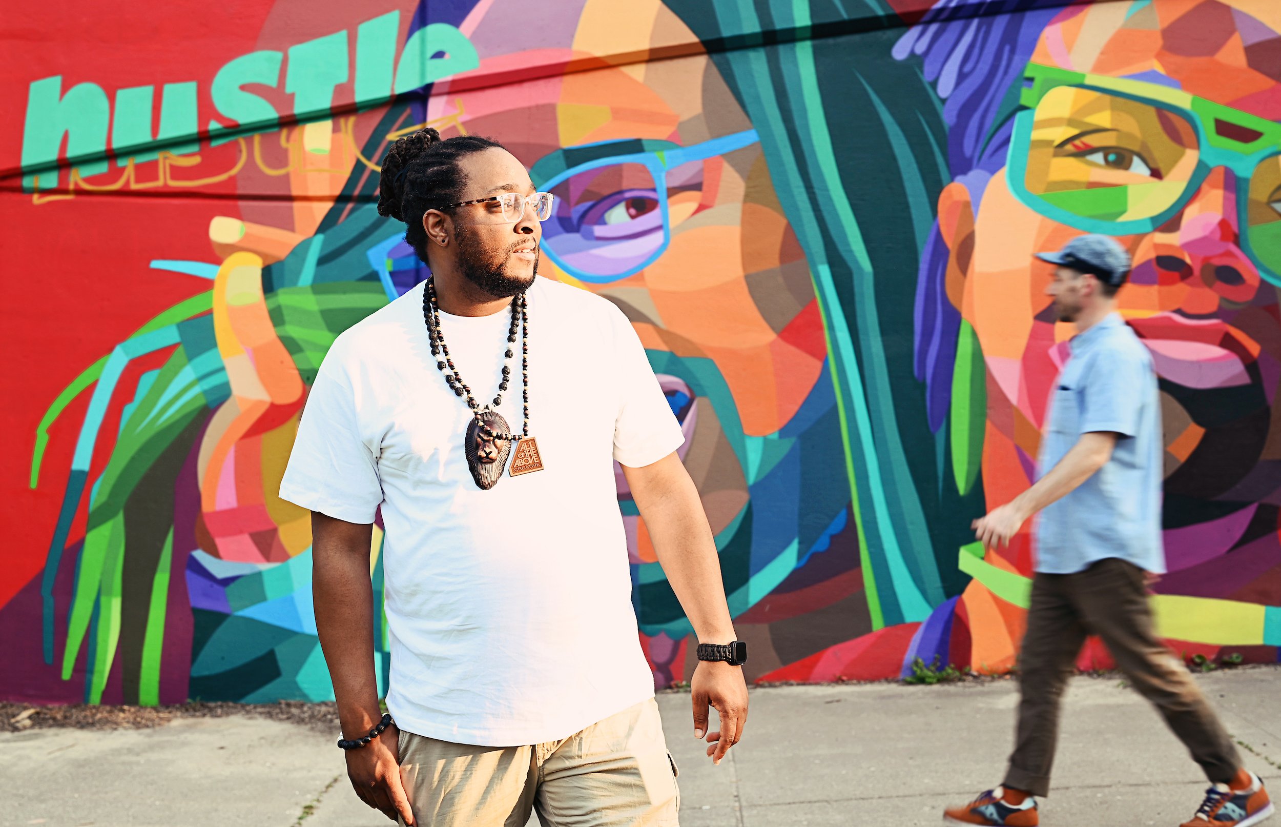  Muralmatics founder Dustin Hunt posing with a Lansing, Michigan resident in front of the mural ‘Hustle &amp; Motivate’ 