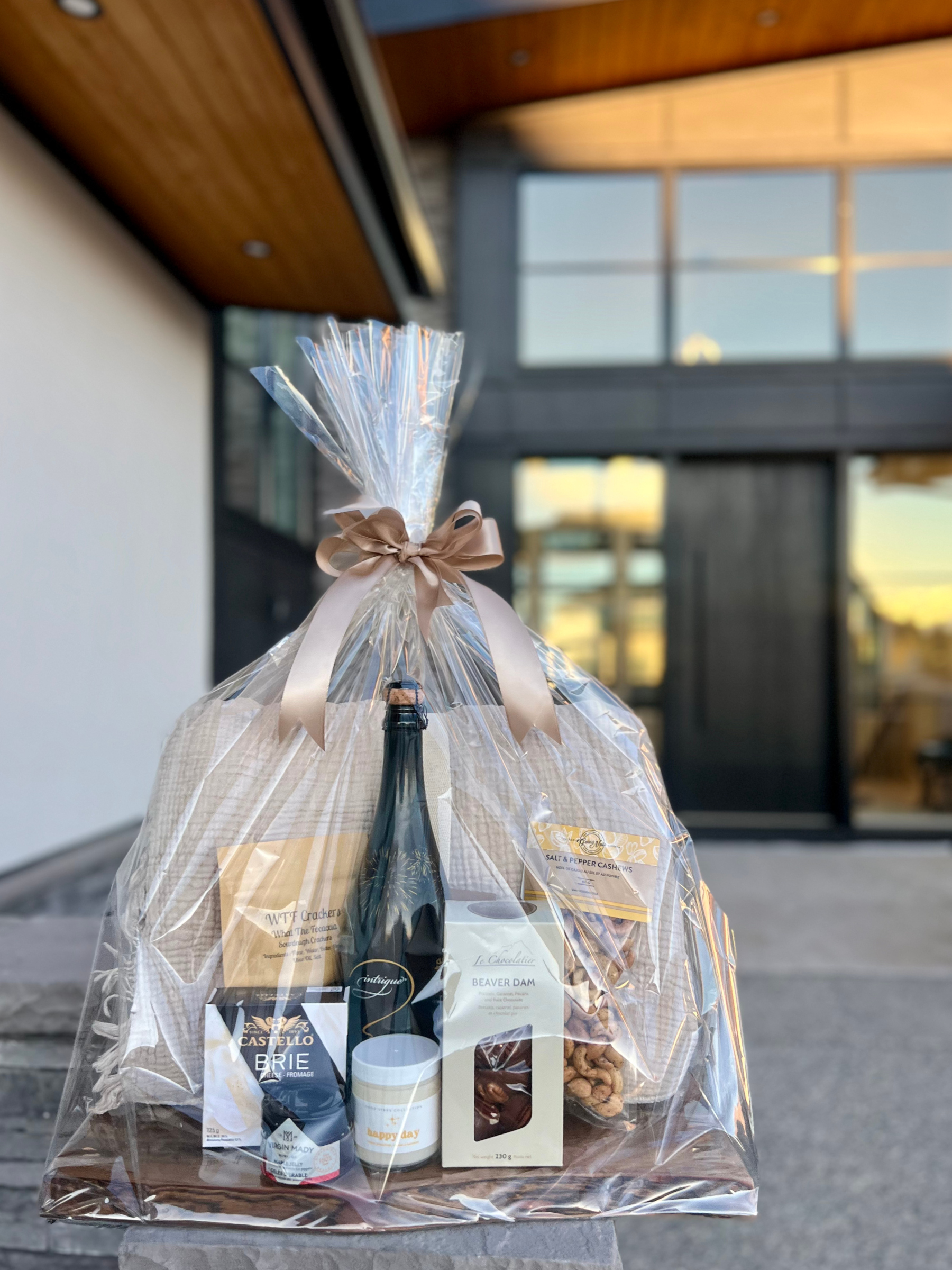 Gift basket containing wine, cheese, crackers, chocolates, nuts, and a small jar.