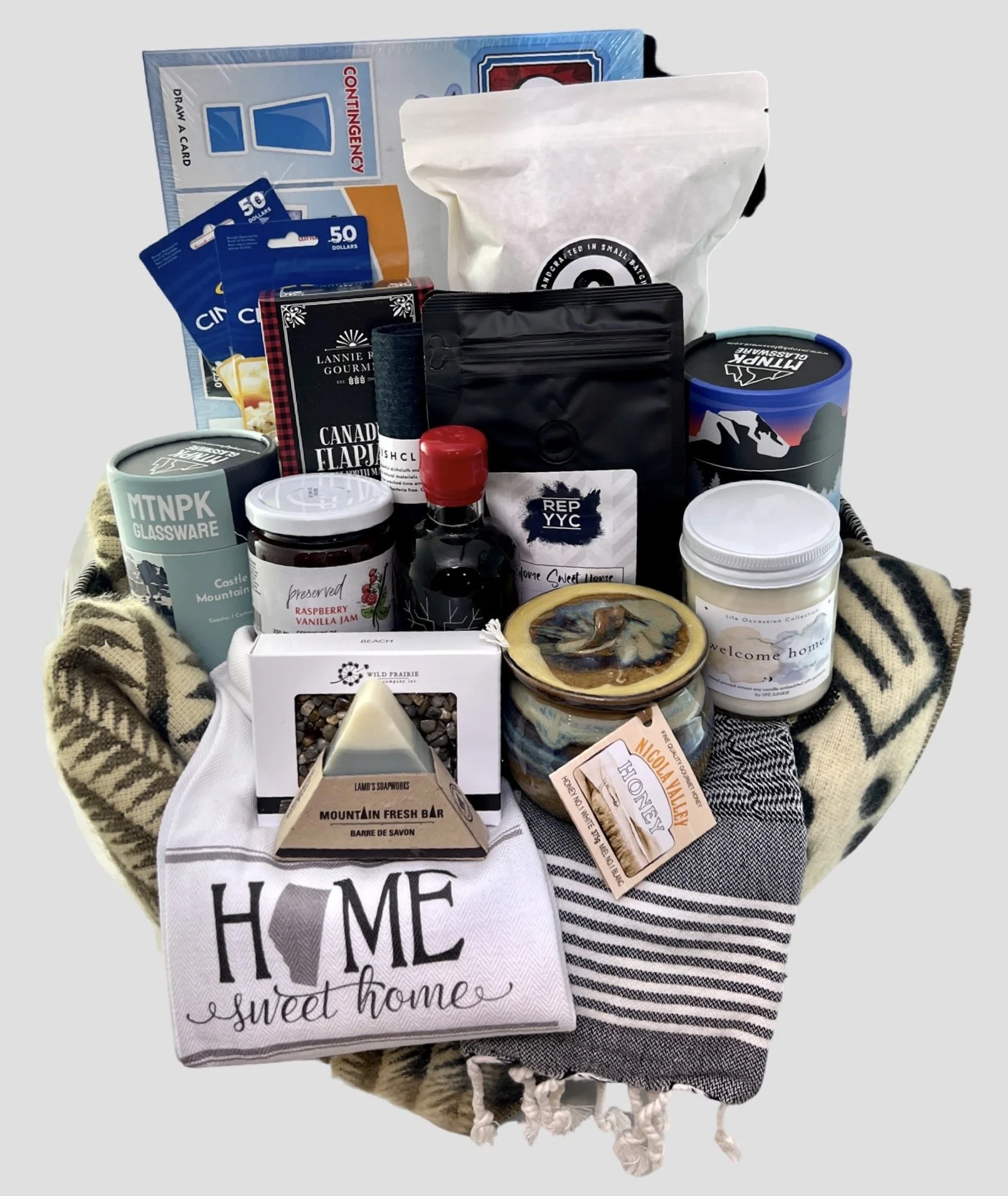 Gift basket containing variety of items such as board game, coffee, jam, honey, soap, candle, and dish towel with 'home sweet home' text.