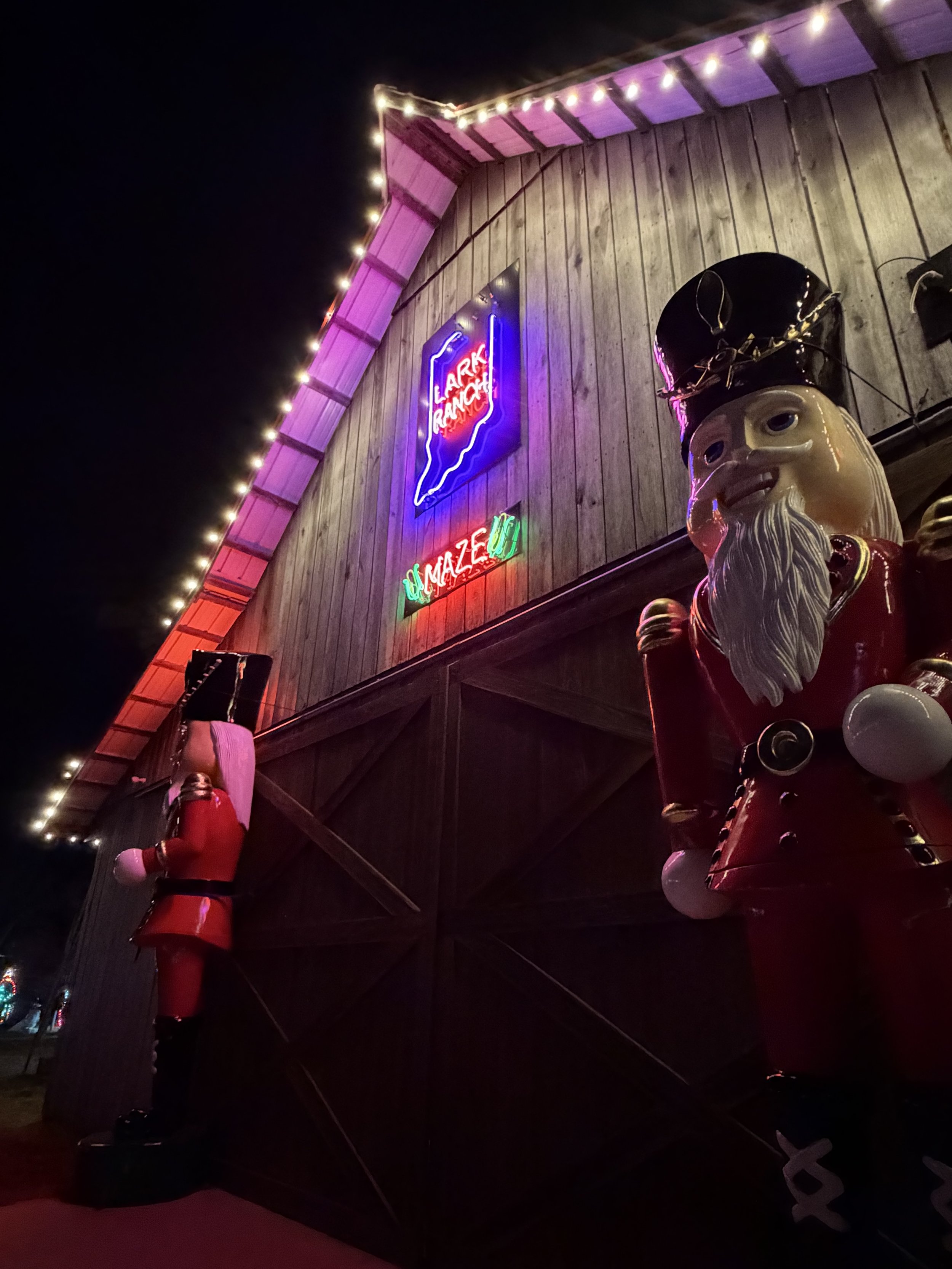 Decorative Santa Claus figures outside a building at night, with colorful neon signs and strings of lights on the wooden exterior wall.