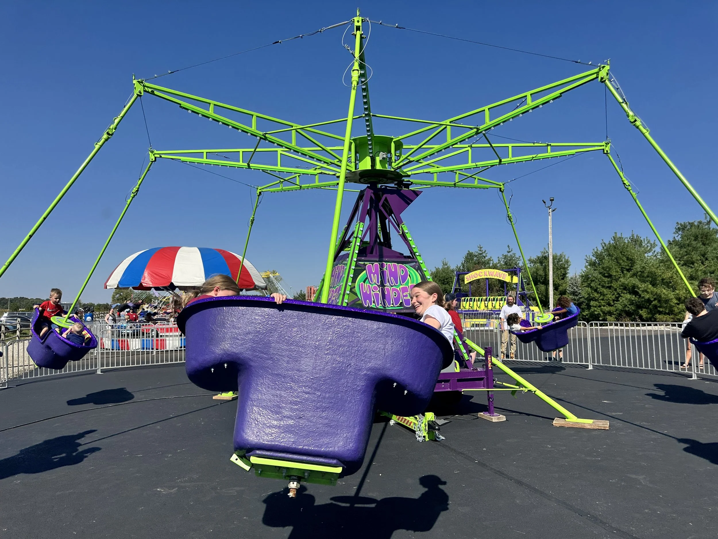 Colorful amusement park ride with seats shaped like large purple cups and a rotating arm structure, featuring children enjoying the ride on a bright sunny day.