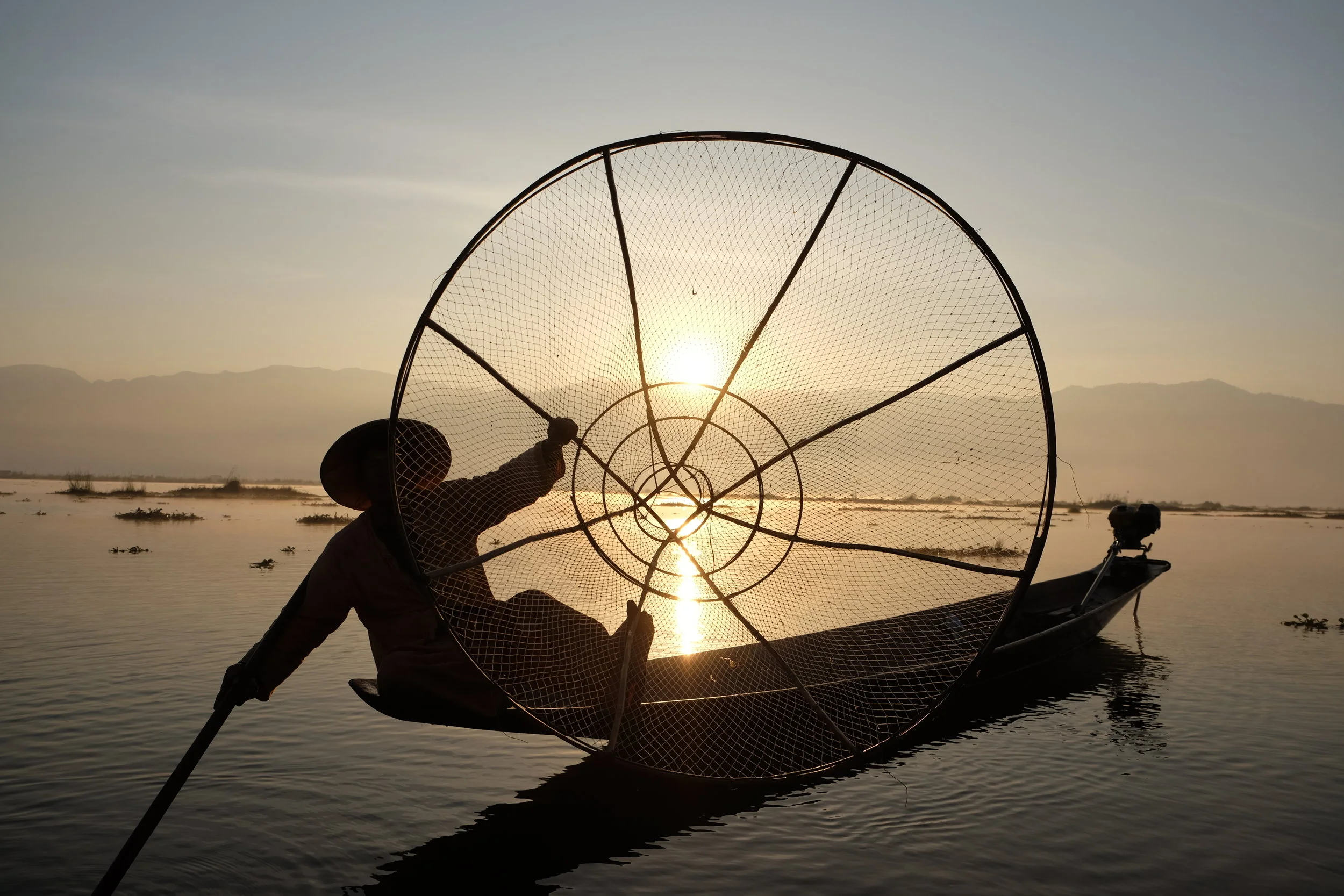 Inle Lake fisherman holding his net up to the camera at sunrise