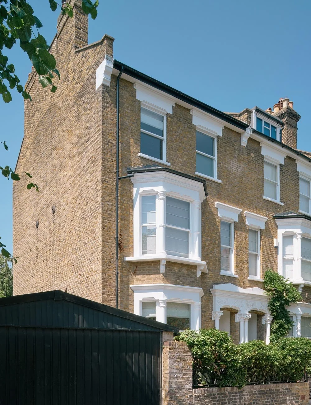 Viktorianskt townhouse från sent 1800-tal i gult tegel med vita fönster, omgivet av grönska i norra London.