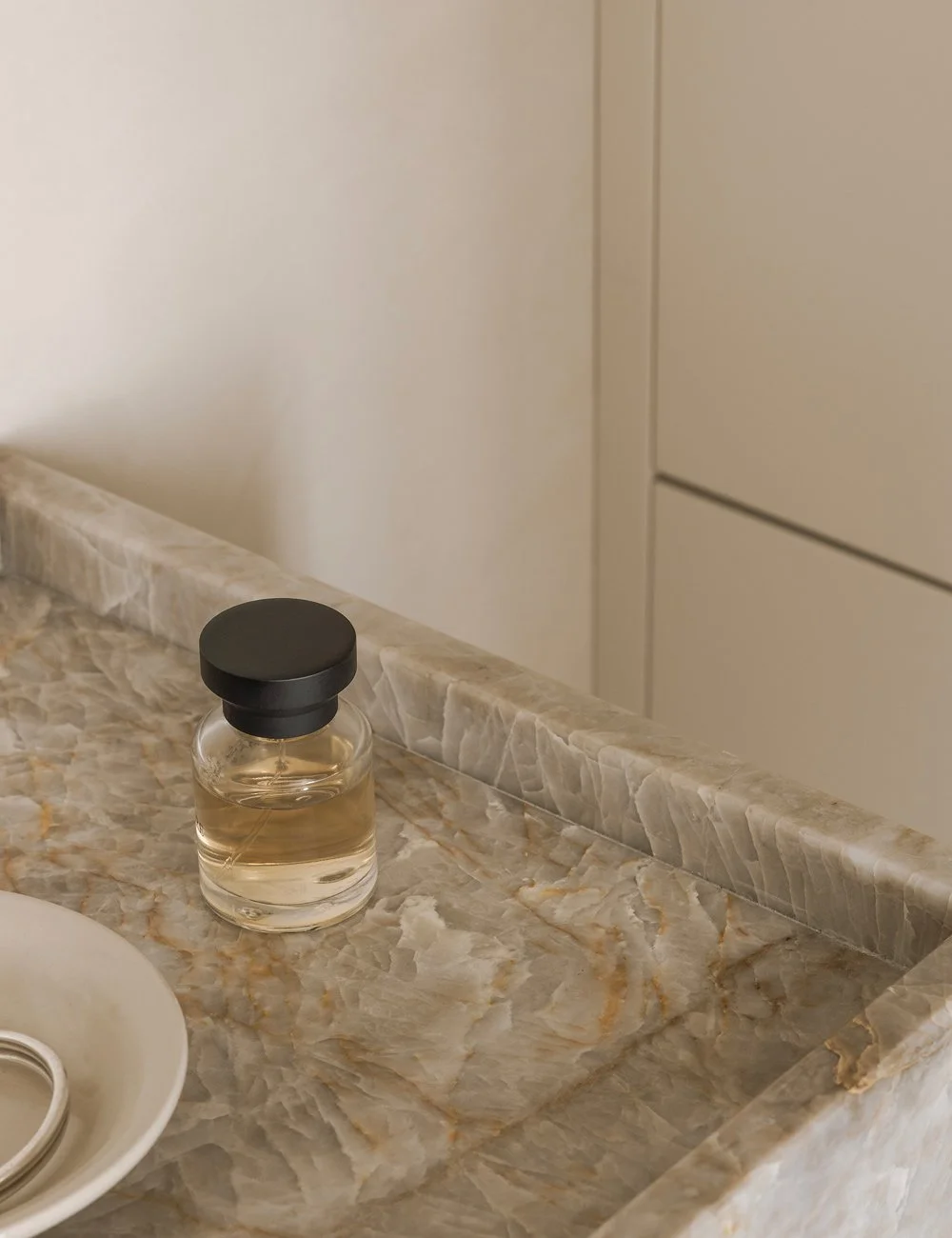 Handfat i natursten av typen taj mahal med toner av bärnsten, beige och mjukt vitt skapar värme i det minimalistiska badrummet.