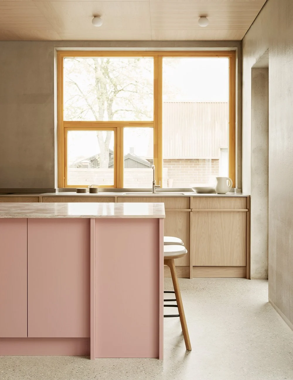 Platsbyggt kök i ljus ek med en mjukt rosa köksö och matchande bänkskiva i rosa marmor.