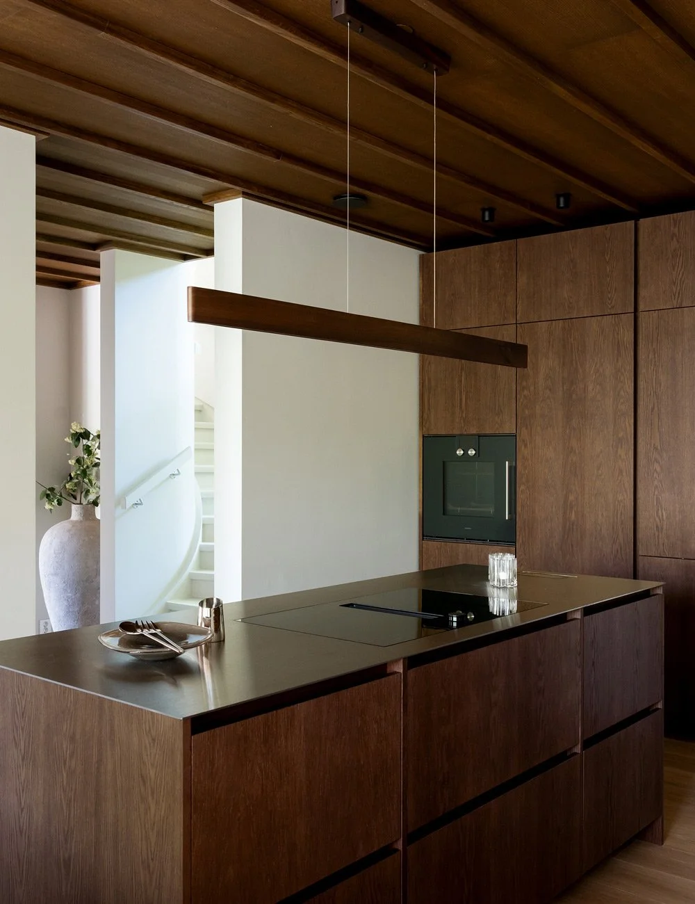 Köksö i mörk ek med bänkskiva i rostfritt stål och högskåp i ett hem inspirerat av Mid-Century Modern.