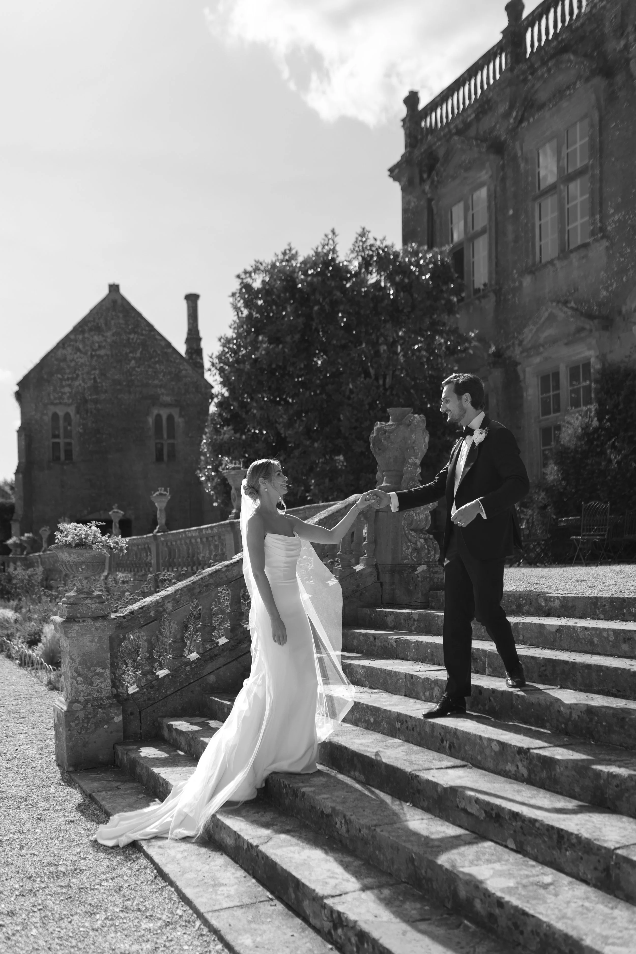 A bride and groom farewel from stairs outside a large historic mansion in black and white