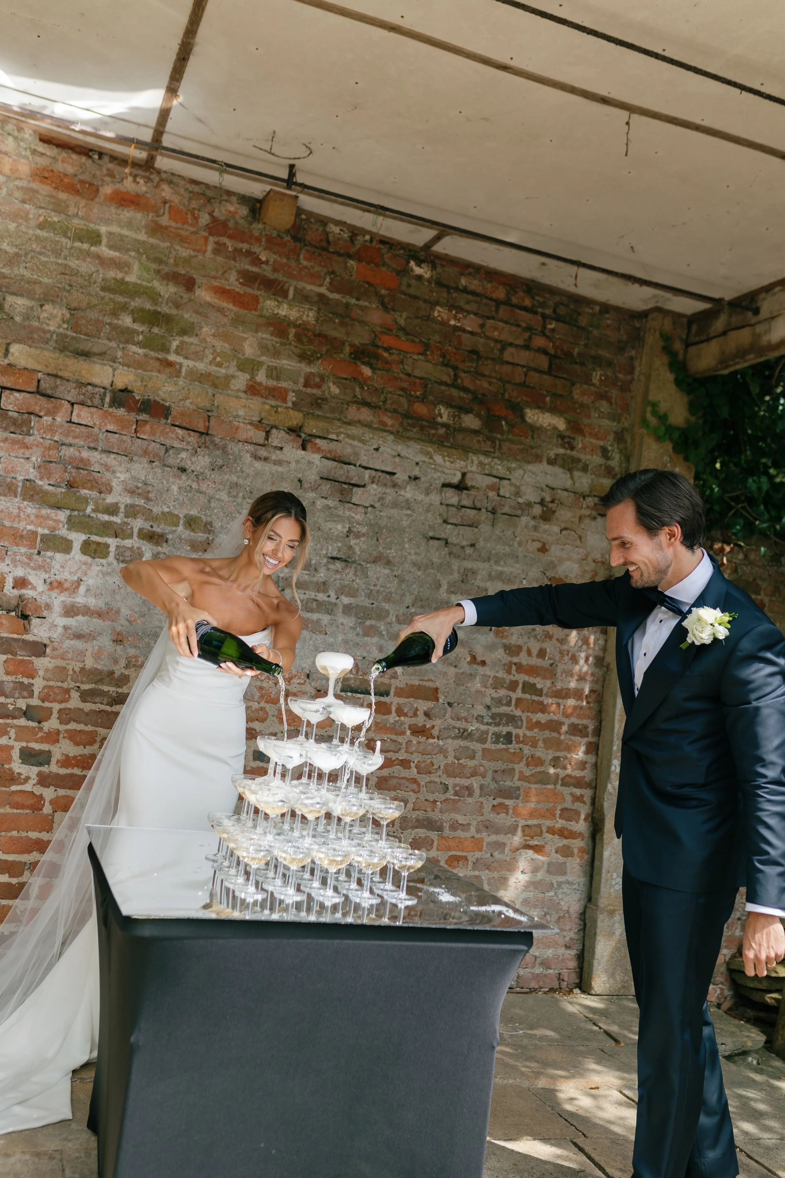 A bride and groom celebrating with a champagne tower at their wedding, pouring champagne into glasses.