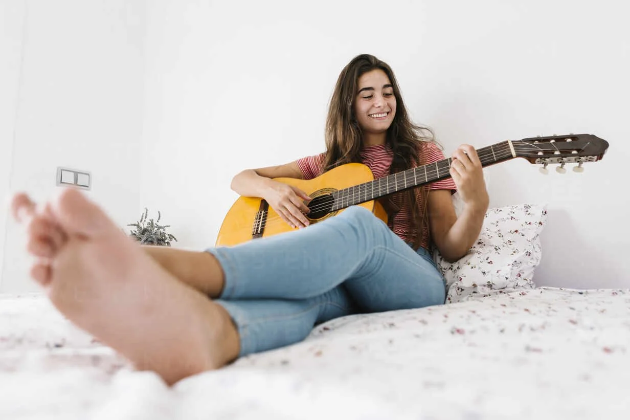 smiling-young-woman-playing-guitar-at-home-in-bedroom-XLGF00543.jpg
