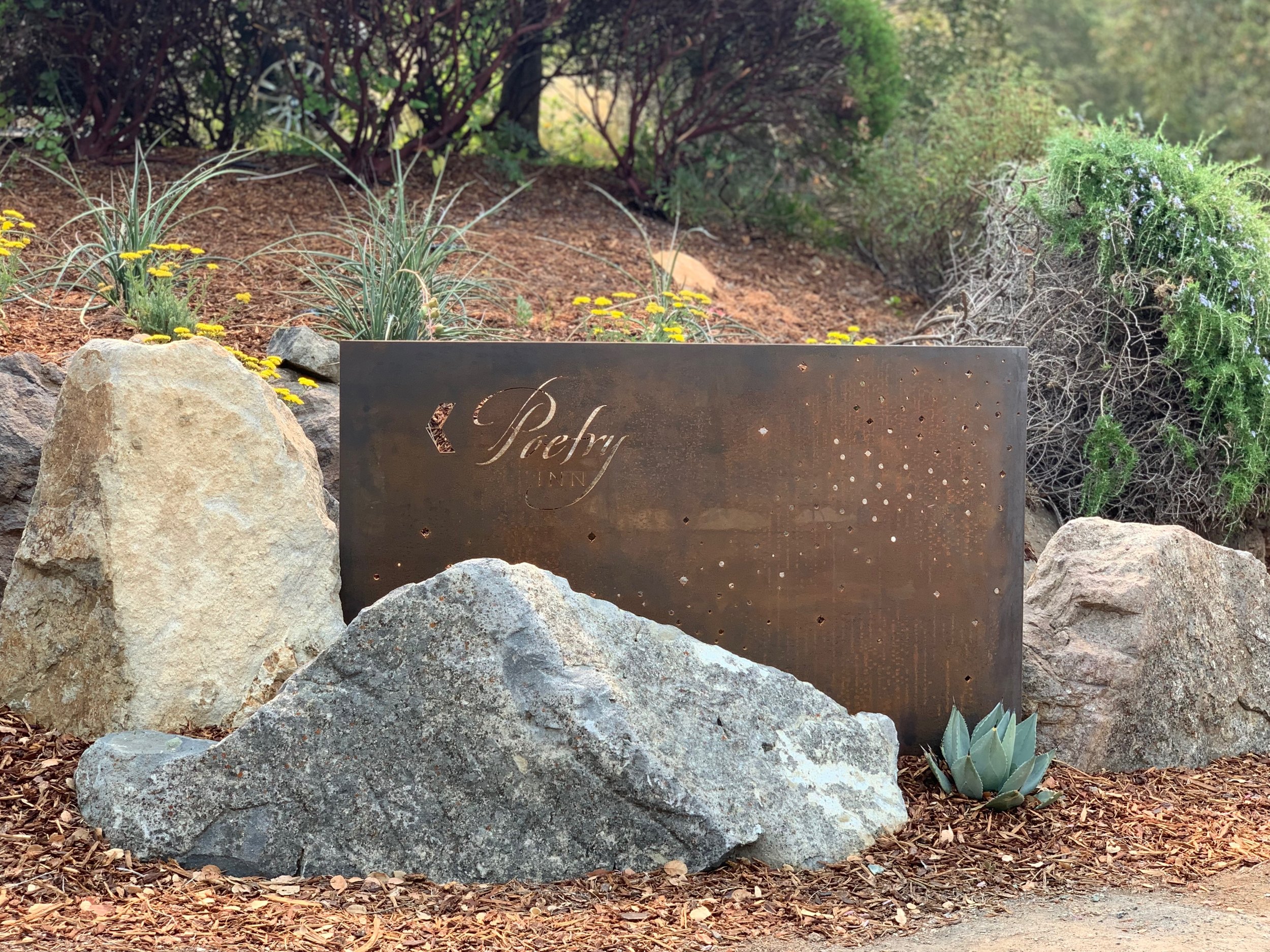Corten steel signage at a key vehicular turn welcome guests and continue the celebration of sky. Rock outcroppings enhance the existing rocky terrain and drought tolerant planting complements the native landscape while providing a pop of color. Com