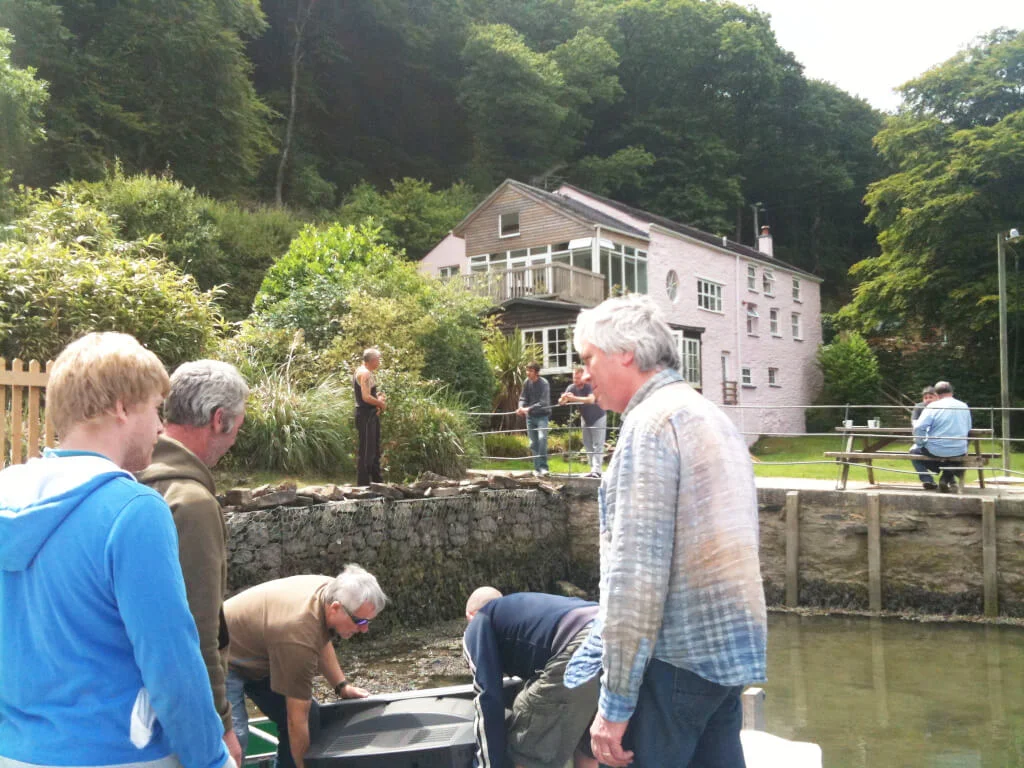 Three people at the water's edge at Sawmills Studio, with the studio building behind