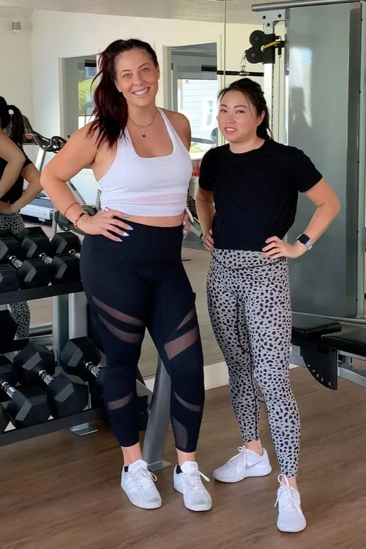 two women in black and white workout clothing standing next to a stand of barbells