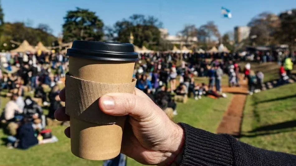 Taza de café descartable sostenida con la mano durante un evento al aire libre, ejemplo del impacto ambiental del consumo de plásticos de un solo uso.