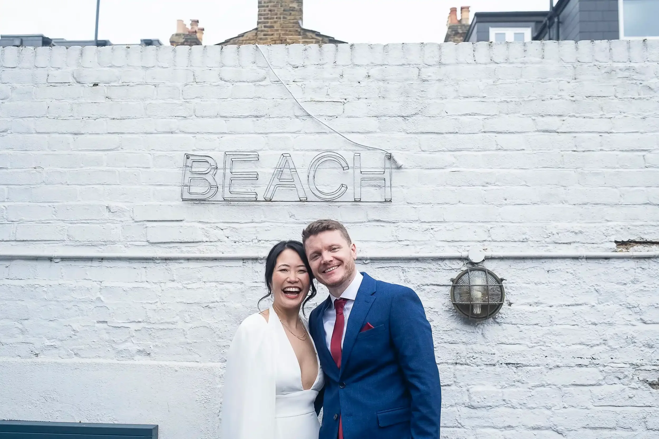 Wedding couple with white brick wall with sign saying BEACH behind them