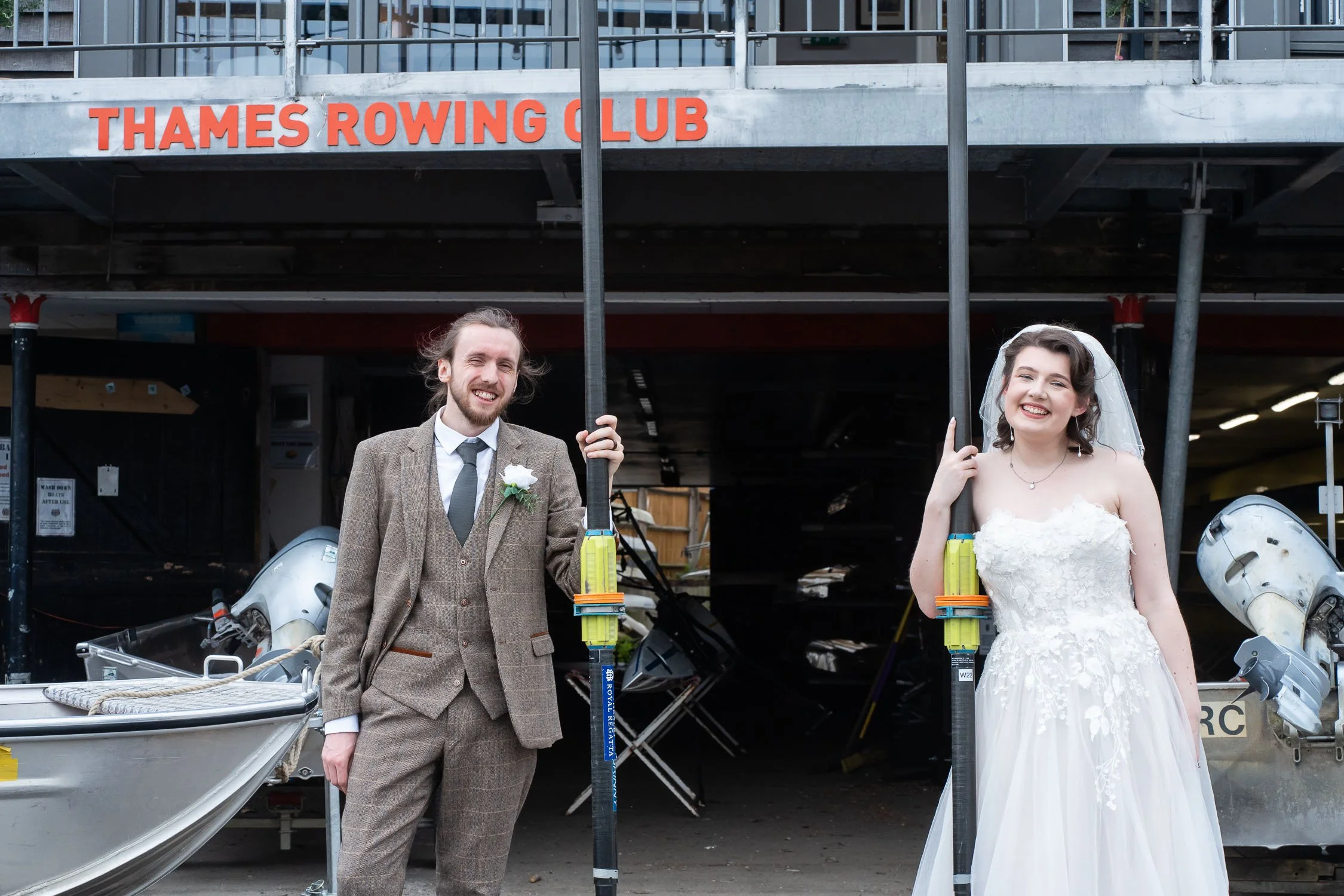 wedding couple standing outside Thames Rowing Club holding oars