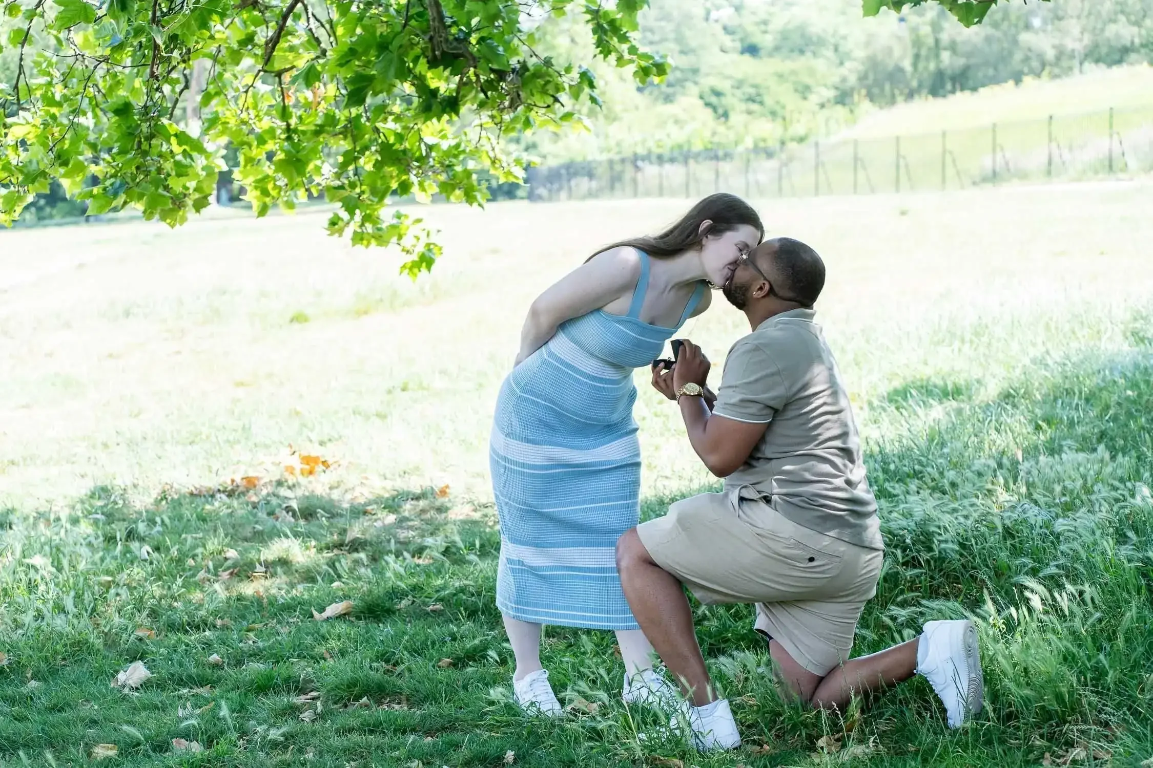 Man on one knee proposing, while woman is kissing him, in a field