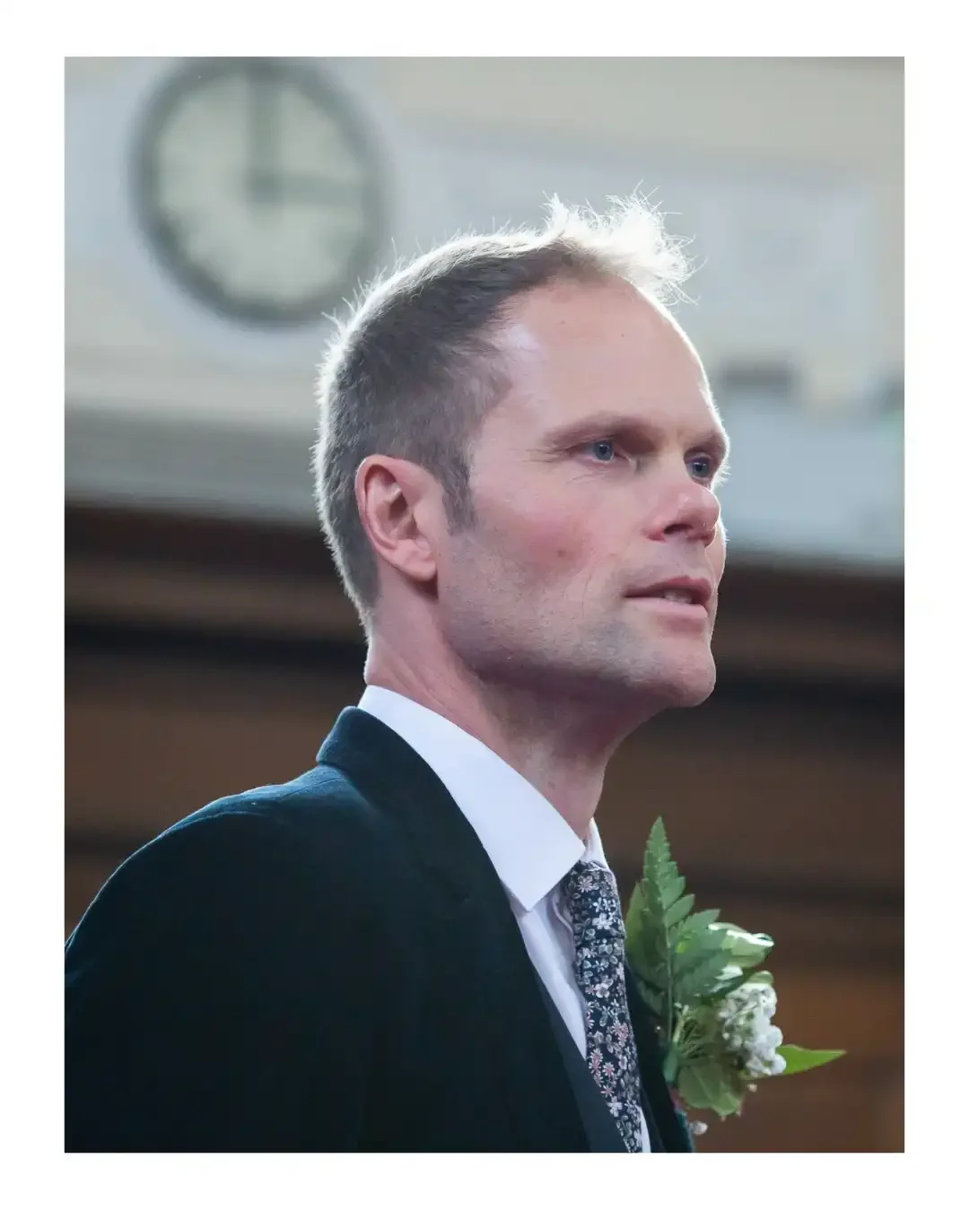 Groom at Islington Town Hall wedding ceremony, looking into middle distance, with clock in background