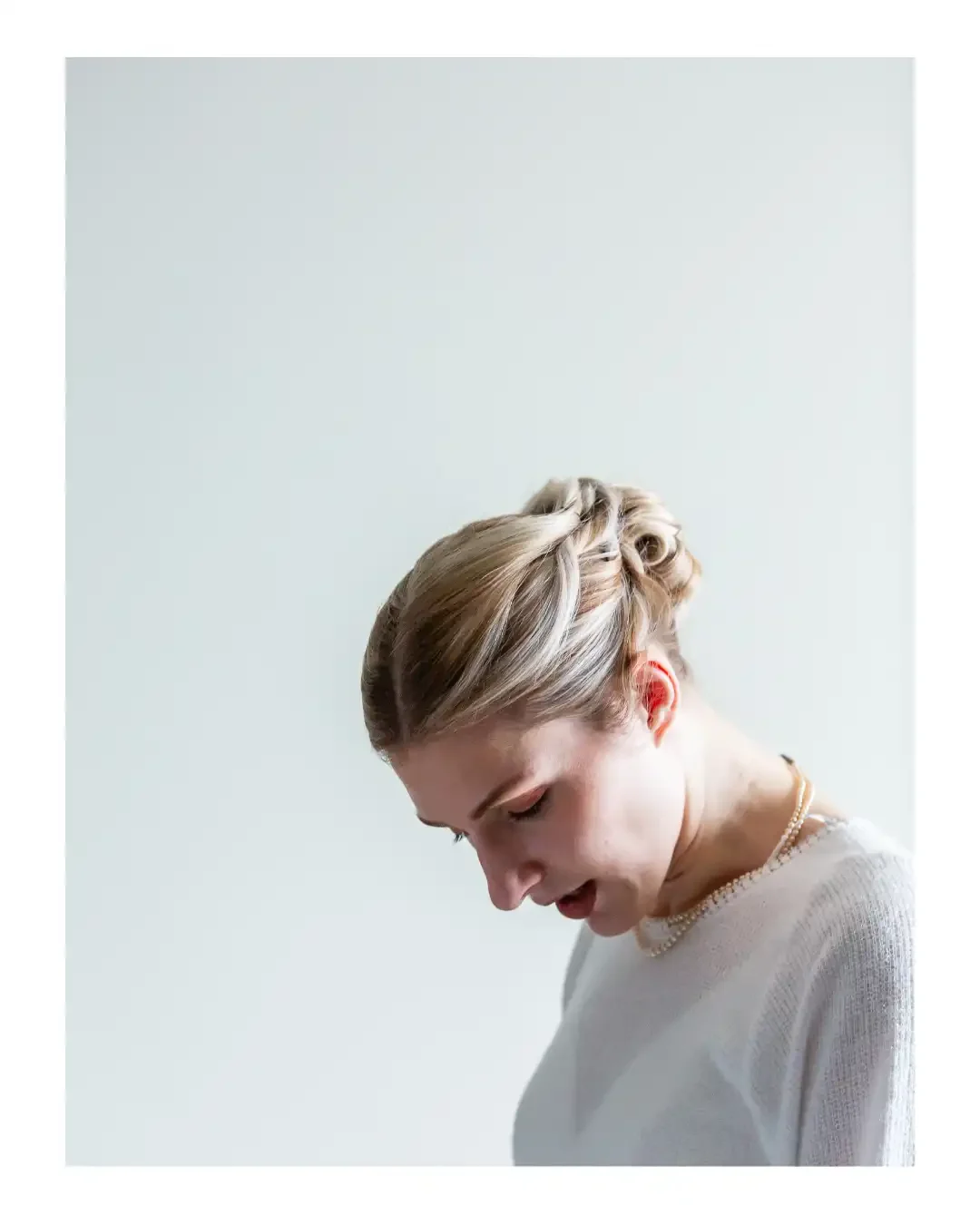 bride looking down at her dress, in front of white wall