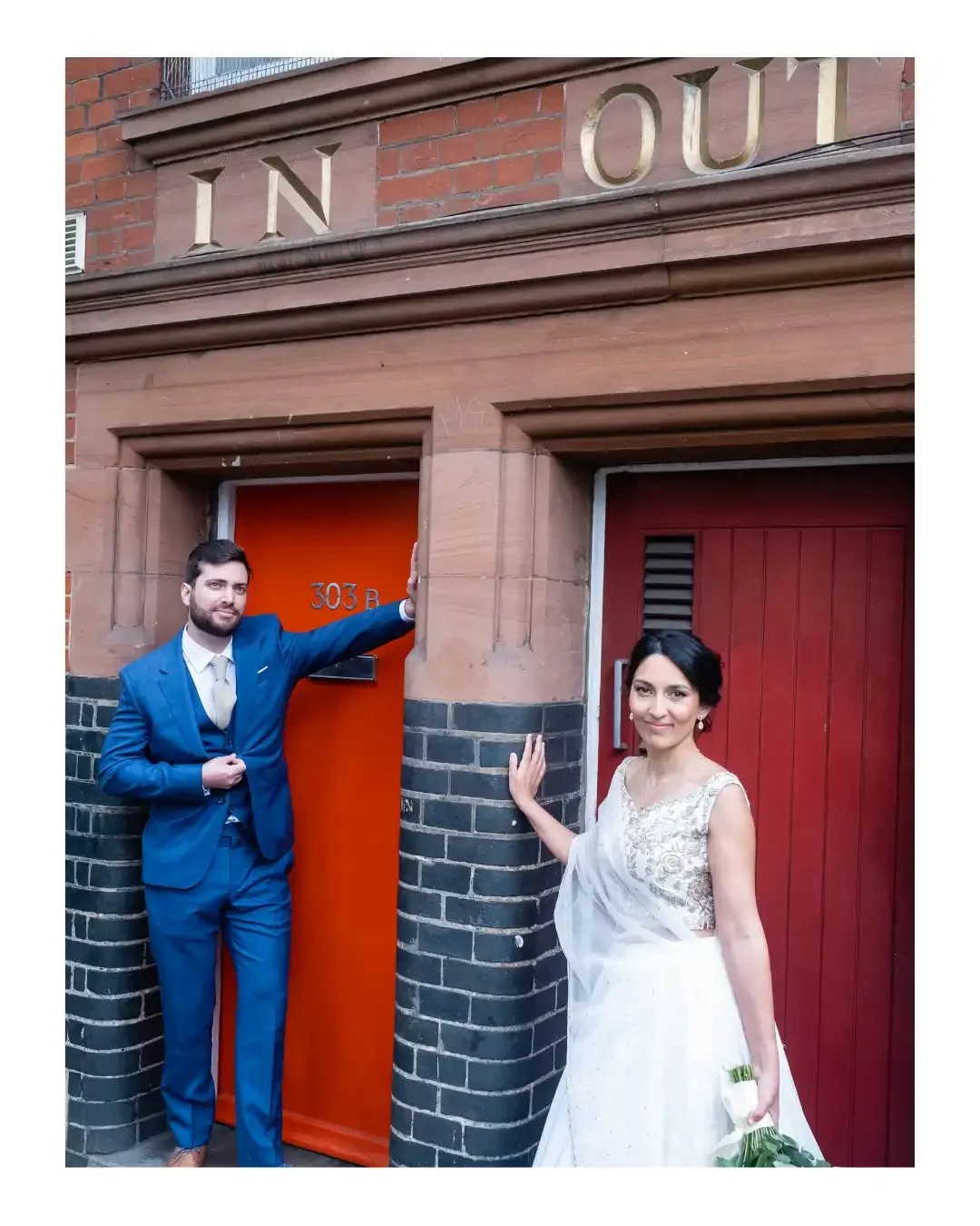 Wedding couple standing in front of 2 red doors, with the sign 'in' and 'out' over both doors