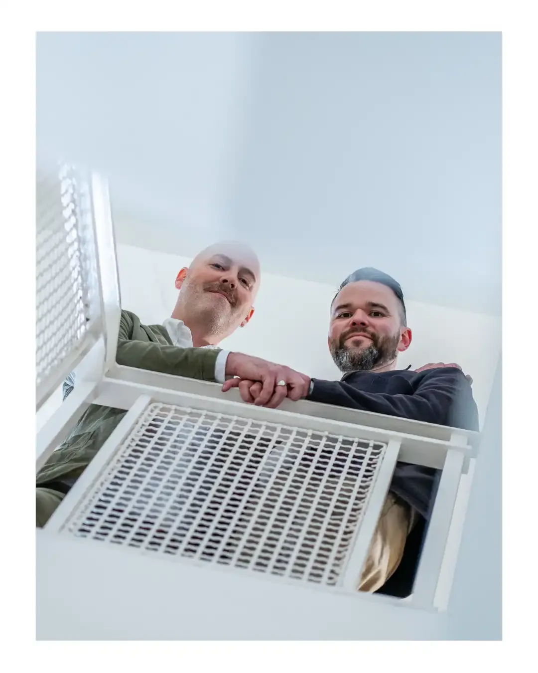 Photo of two men looking down a stairwell, smiling at the camera