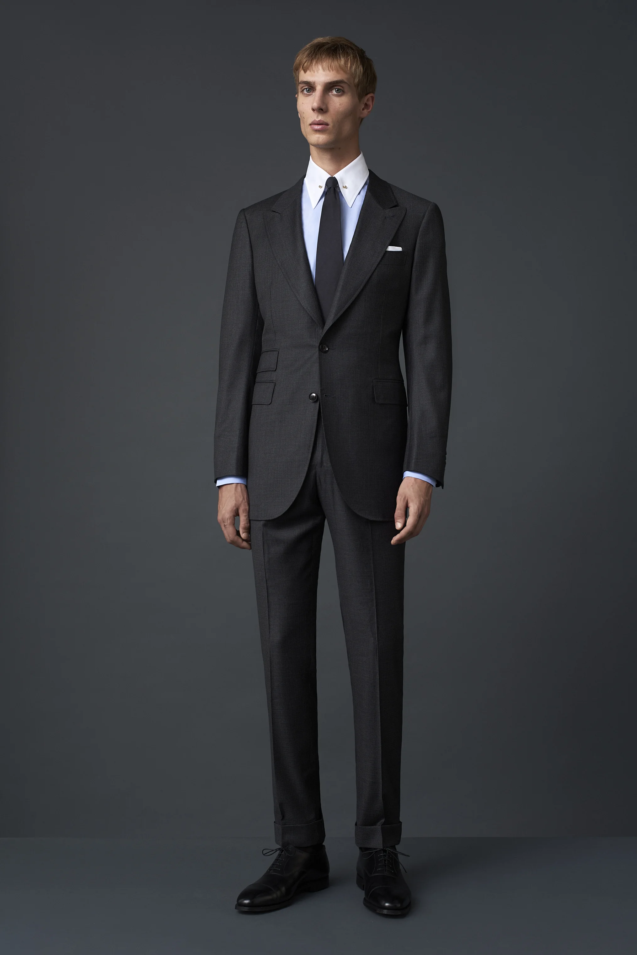 Deep grey suit with a micro houndstooth pattern, with a wide peak lapel, two button closure and a ticket pocket, from S150 merino wool woven in Biella. Paired with an Egyptian cotton shirt with a pin collar and a mid grey silk tie made in Como.