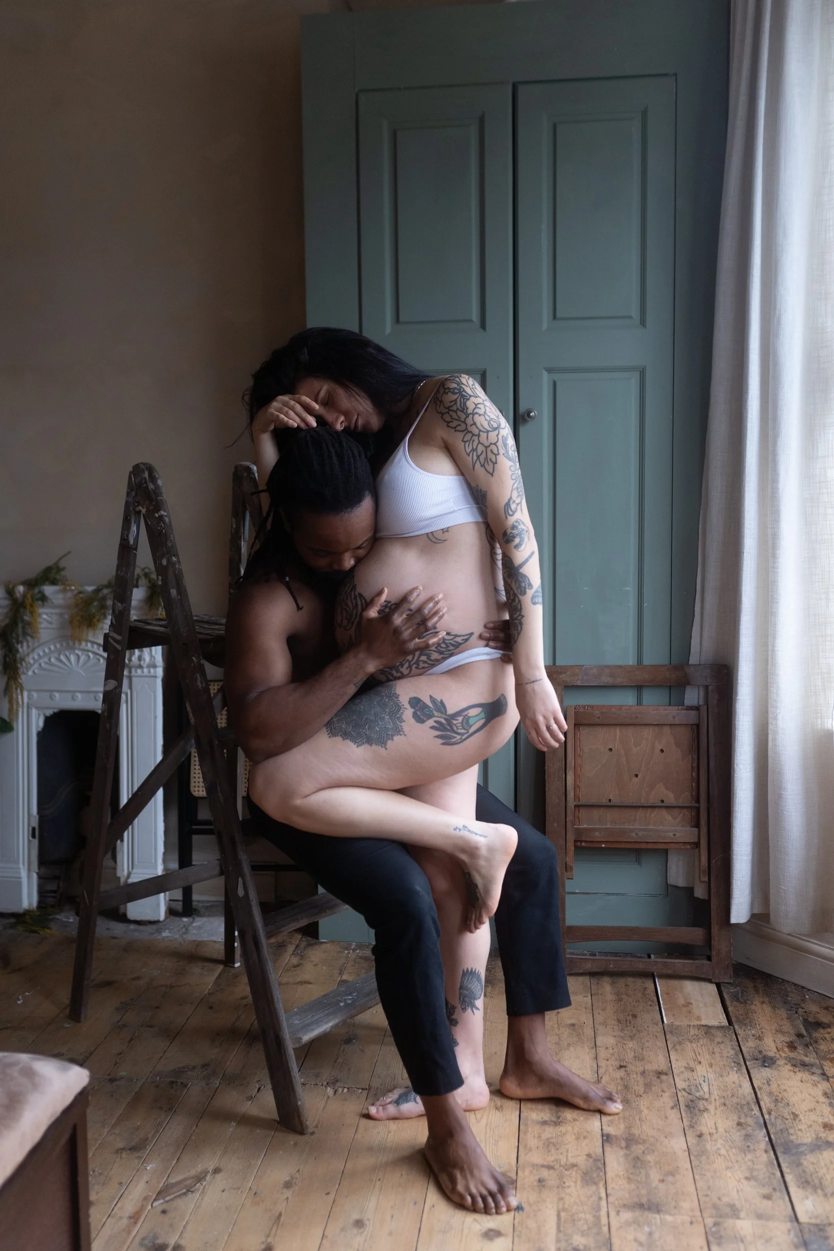 Photo of pregnant woman and a man kissing her stomach whilst seated on a wooden ladder edited with Archipelago Lightroom Presets
