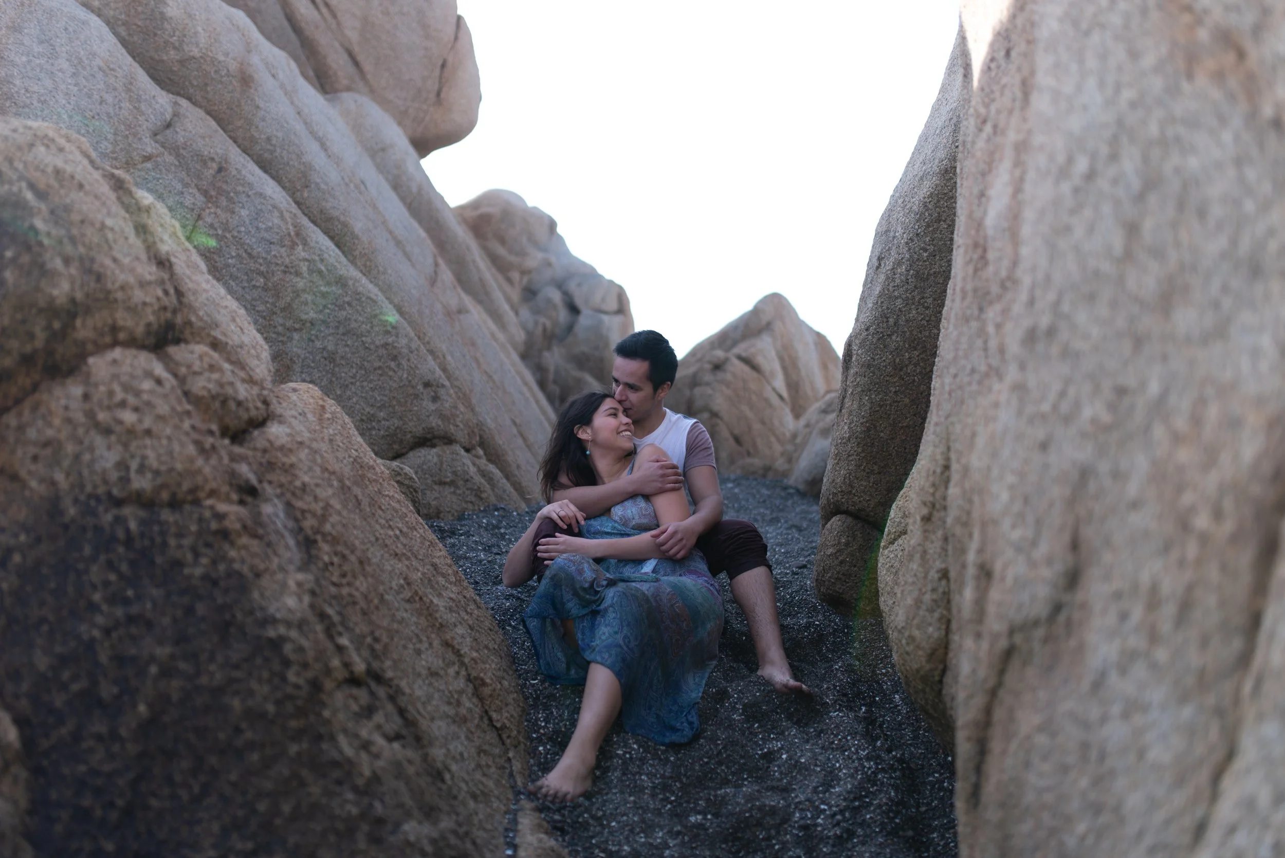 Photo of man and woman seated on the sand between large coastal rock formations edited with Archipelago Lightroom Presets