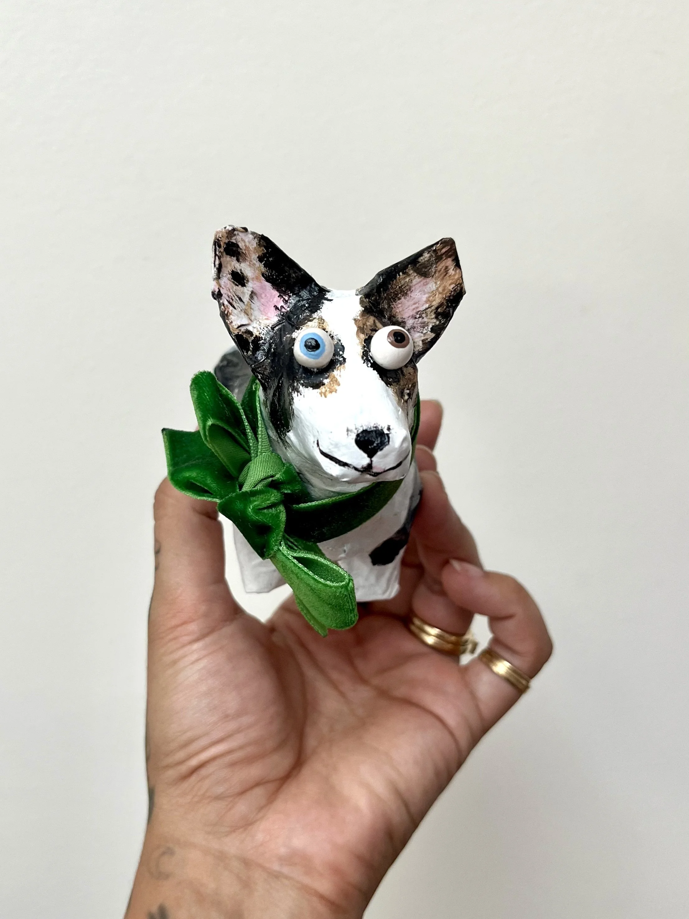 paper mache dog sculpture of corgi with one blue eye and one brown eye wearing a green bow smiling