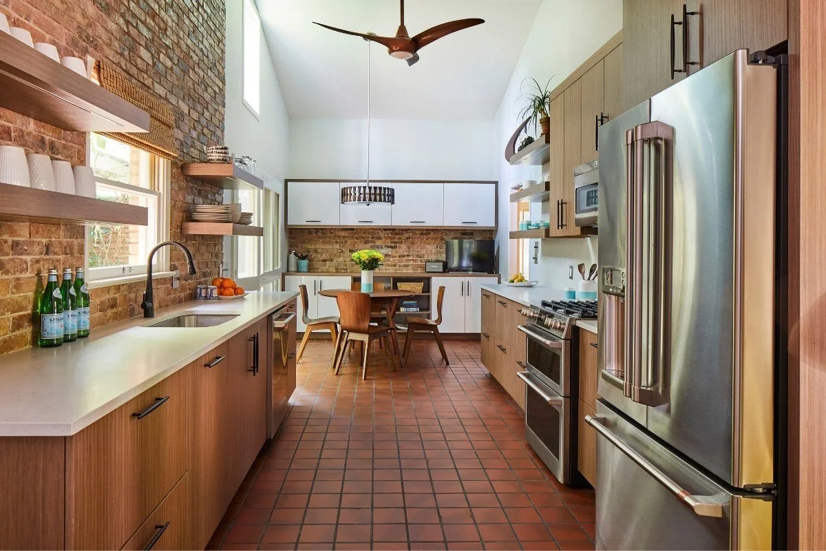 Modern kitchen with exposed brick backsplash, warm wood cabinetry, floating shelves and stainless steel appliances