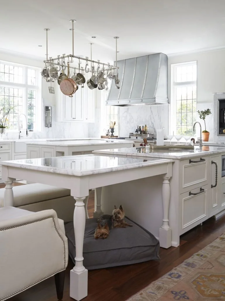 Large white kitchen with two islands, custom cabinetry, marble countertops and integrated appliances