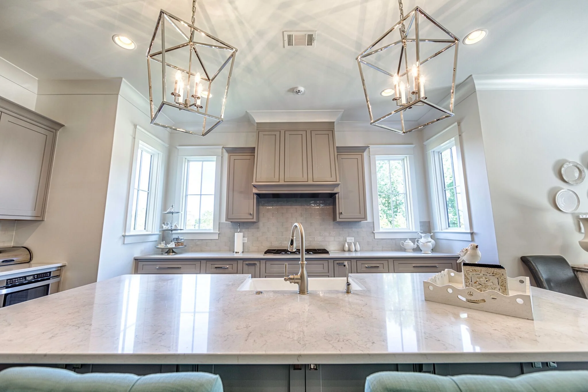 Bright kitchen with taupe cabinetry, a built-in range hood, quartz countertops, and two glass pendant lights.