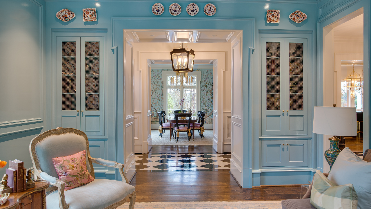 Elegant living space featuring custom sky blue built-in cabinetry with mesh cabinet doors, decorative plate display, traditional millwork, and views into a formal dining room in a luxury Alabama home.