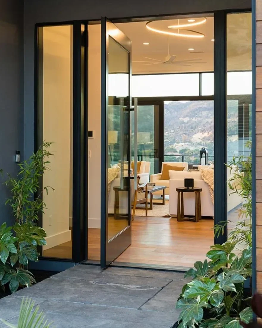 Contemporary pivot entry door with slim black frames and expansive glass panels, offering a modern entrance with abundant natural light.