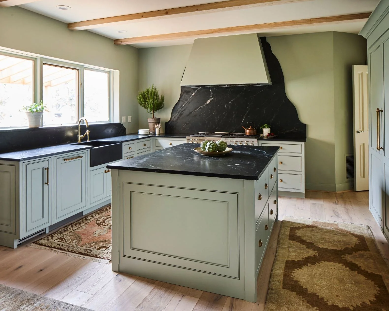 Green custom kitchen island with deep storage drawers and dark stone countertop