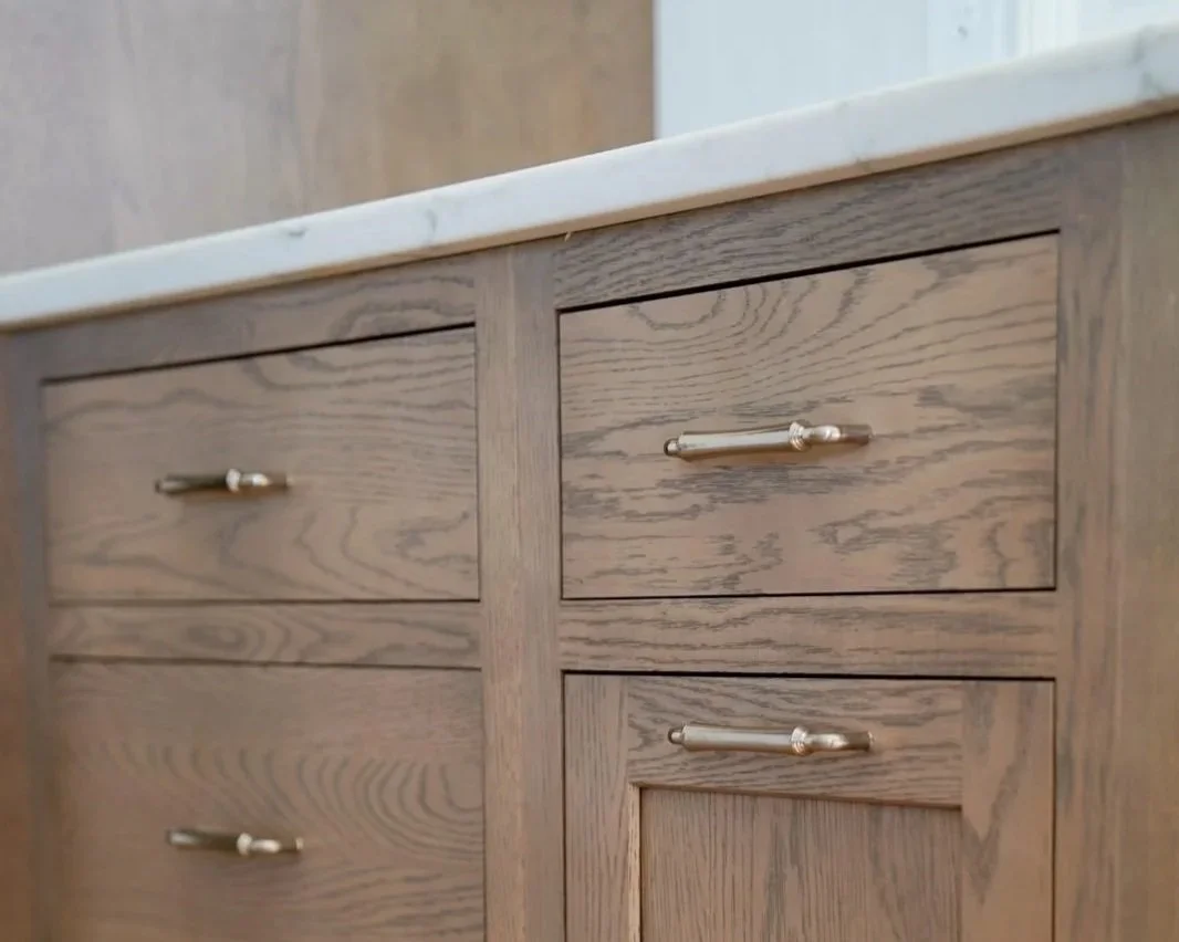 Detailed view of custom white oak kitchen cabinetry with a natural stained finish, showcasing the contrast between slab drawer fronts and shaker-style cabinet doors paired with warm brass pulls.