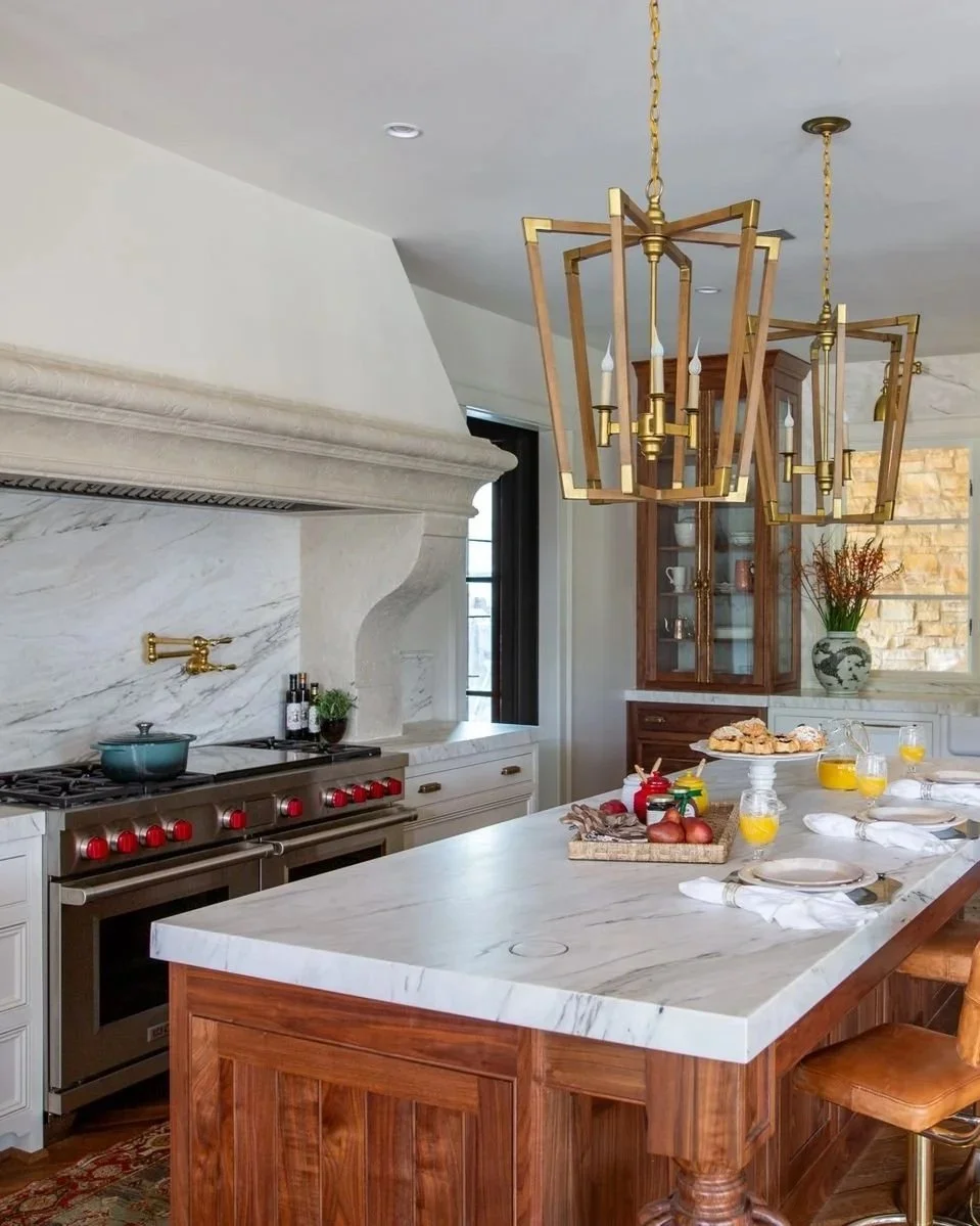 Luxury kitchen featuring a stained walnut island with furniture-style detailing, white custom cabinetry, a marble range backsplash, plaster vent hood, brass lantern pendants, and a professional Wolf range in a high-end Tuscaloosa home.