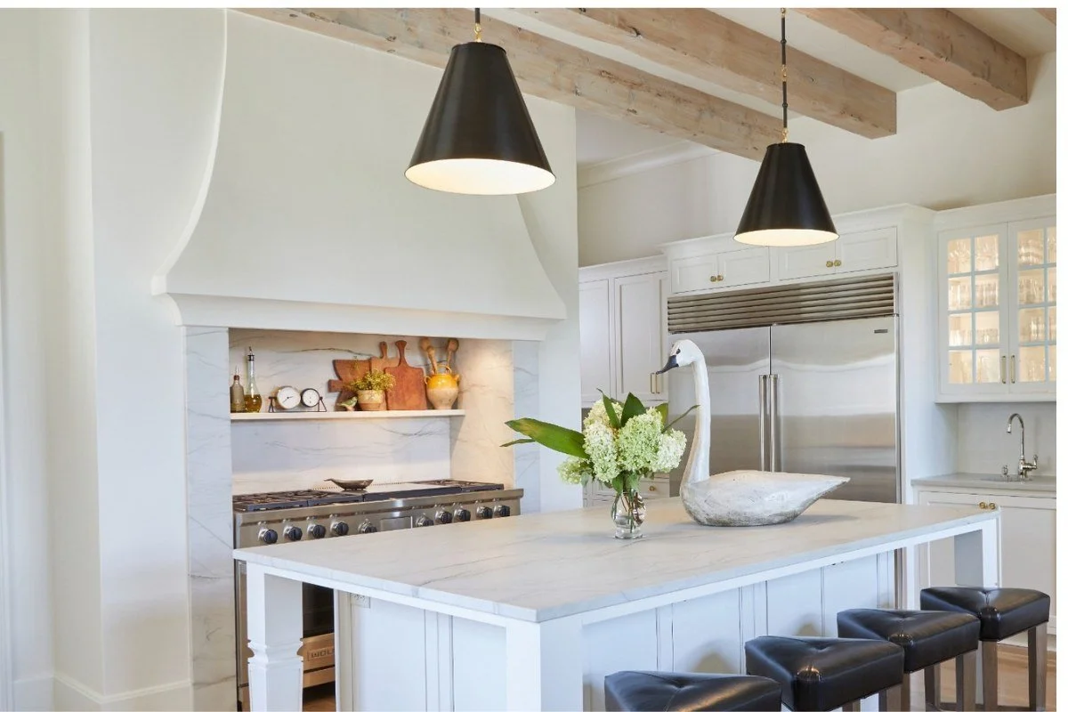 White kitchen with dramatic stone slab backsplash behind the range, brass lantern pendants and wood counter stools