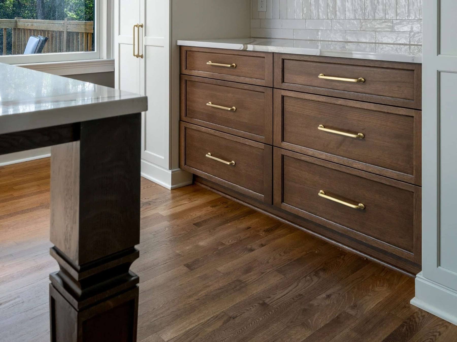 Hardwood kitchen flooring paired with custom dark wood cabinetry and brass hardware in a Tuscaloosa home.