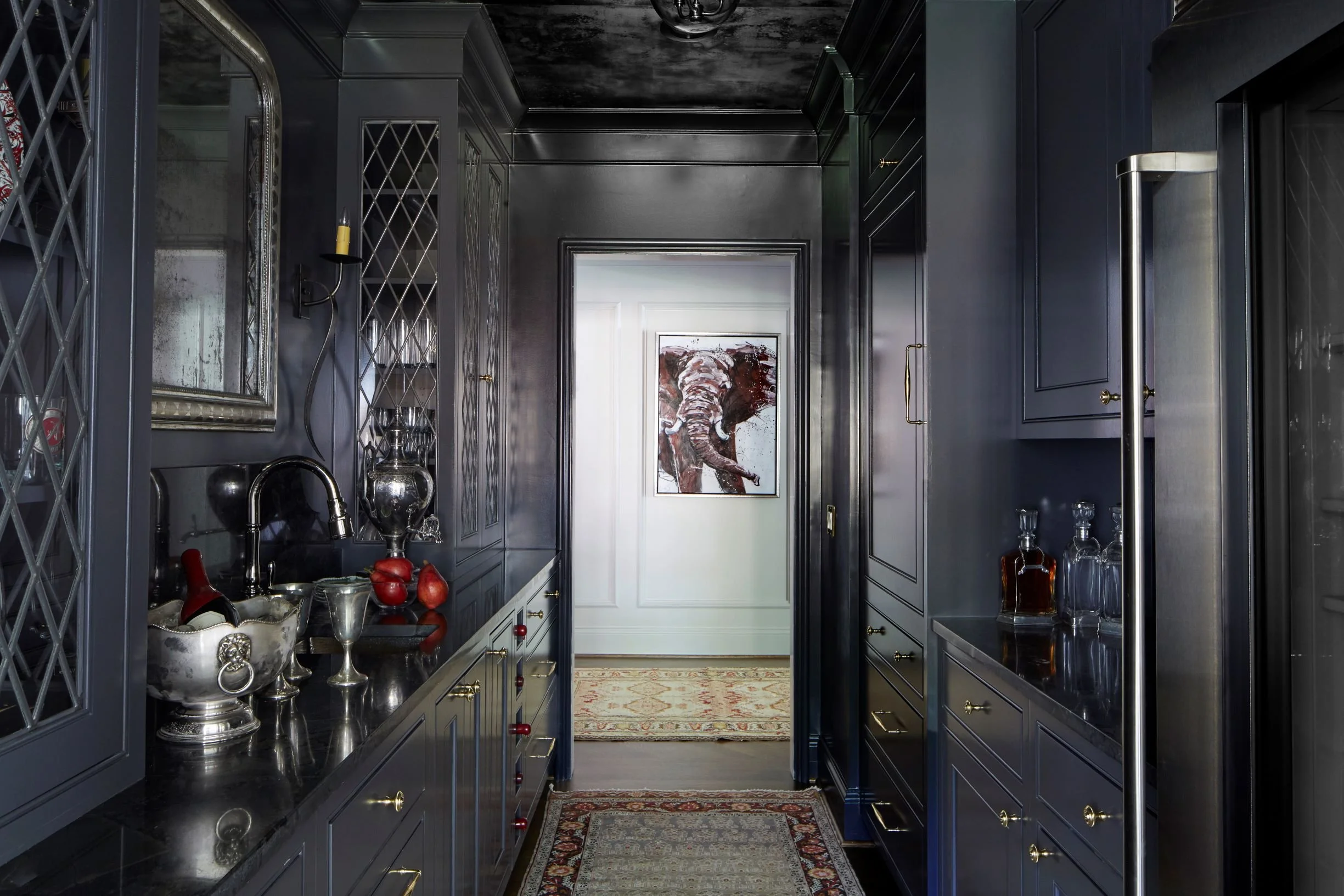 Luxury butler’s pantry featuring dark navy custom cabinetry, black countertops, brass hardware, lattice glass cabinet doors, and dramatic moody finishes in a Birmingham-area home.