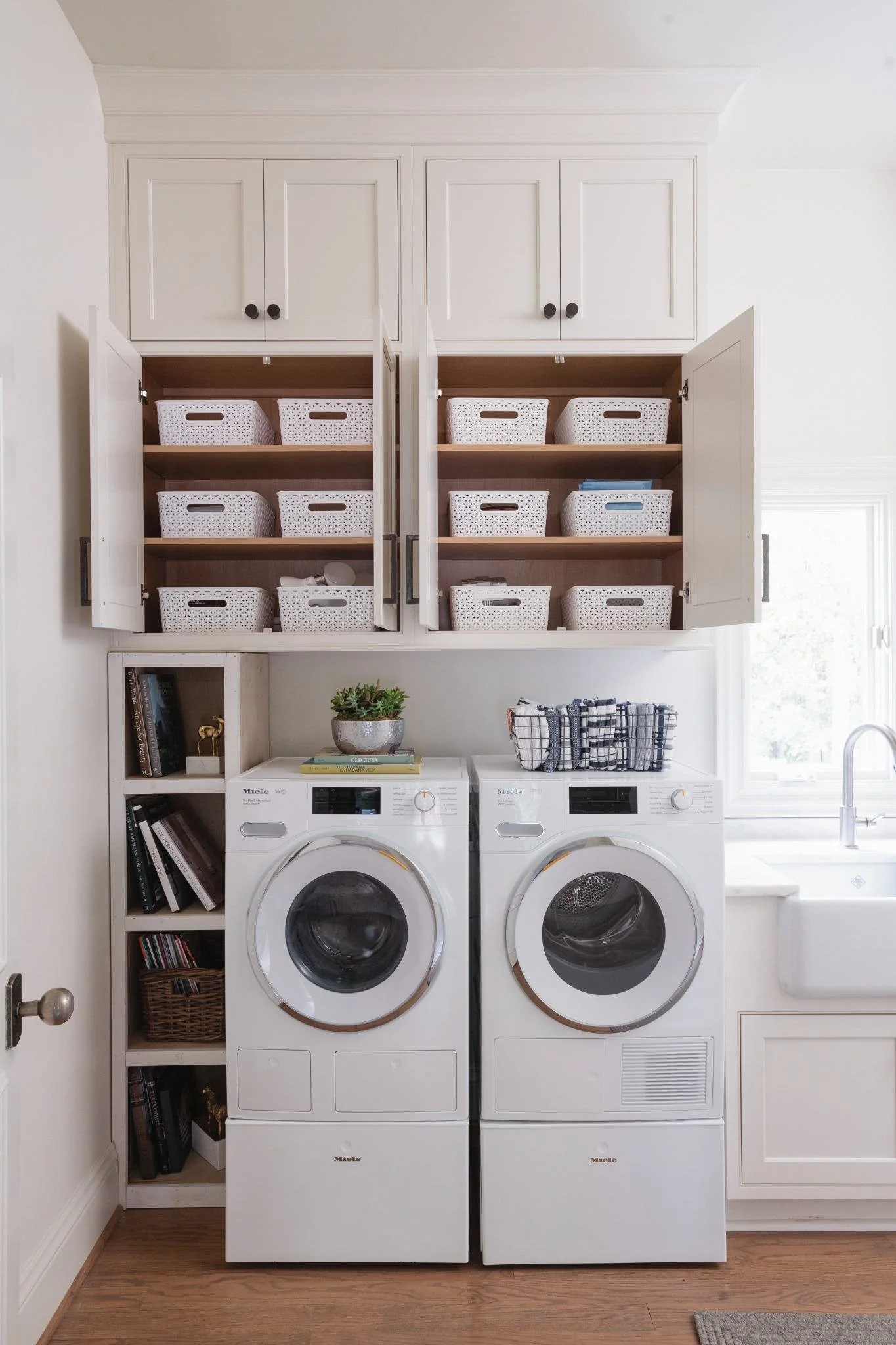 Laundry room featuring white custom cabinetry, front-loading washer and dryer, farmhouse sink and tall storage cabinets.