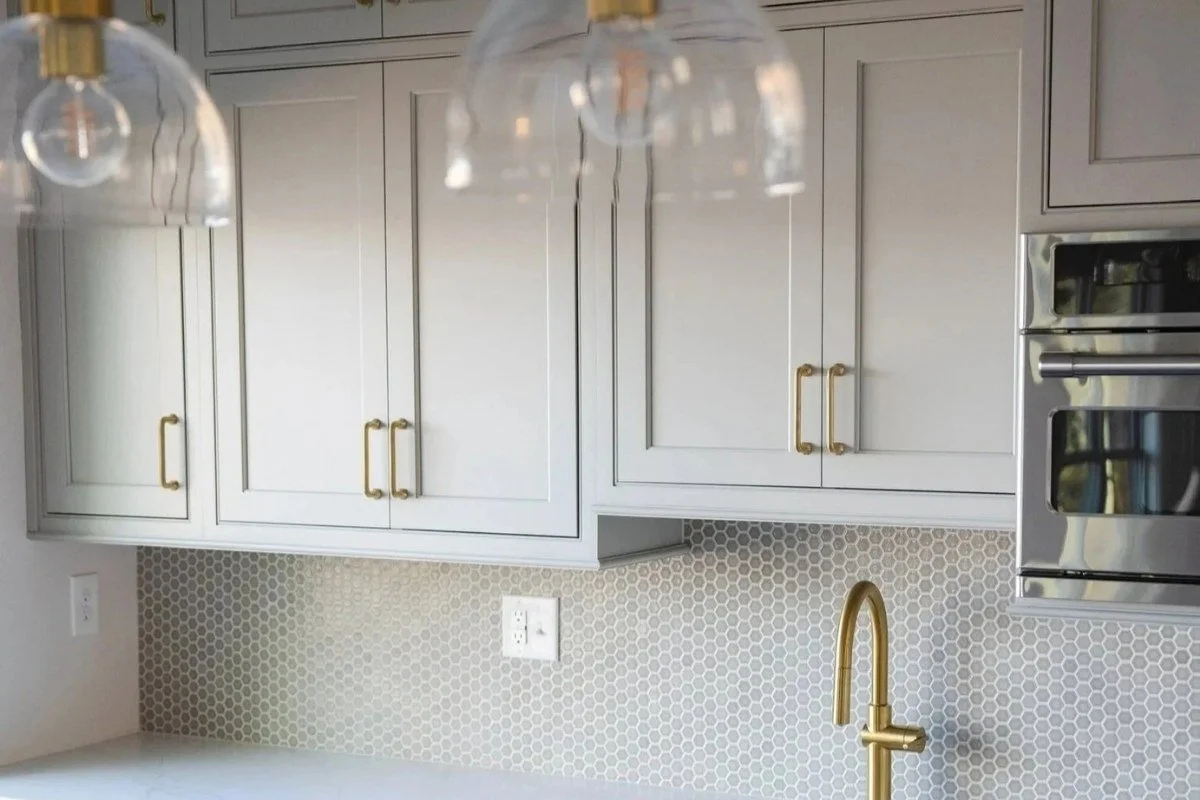 Small gray hexagon mosaic tile backsplash with light gray cabinetry, brass hardware and brass faucet