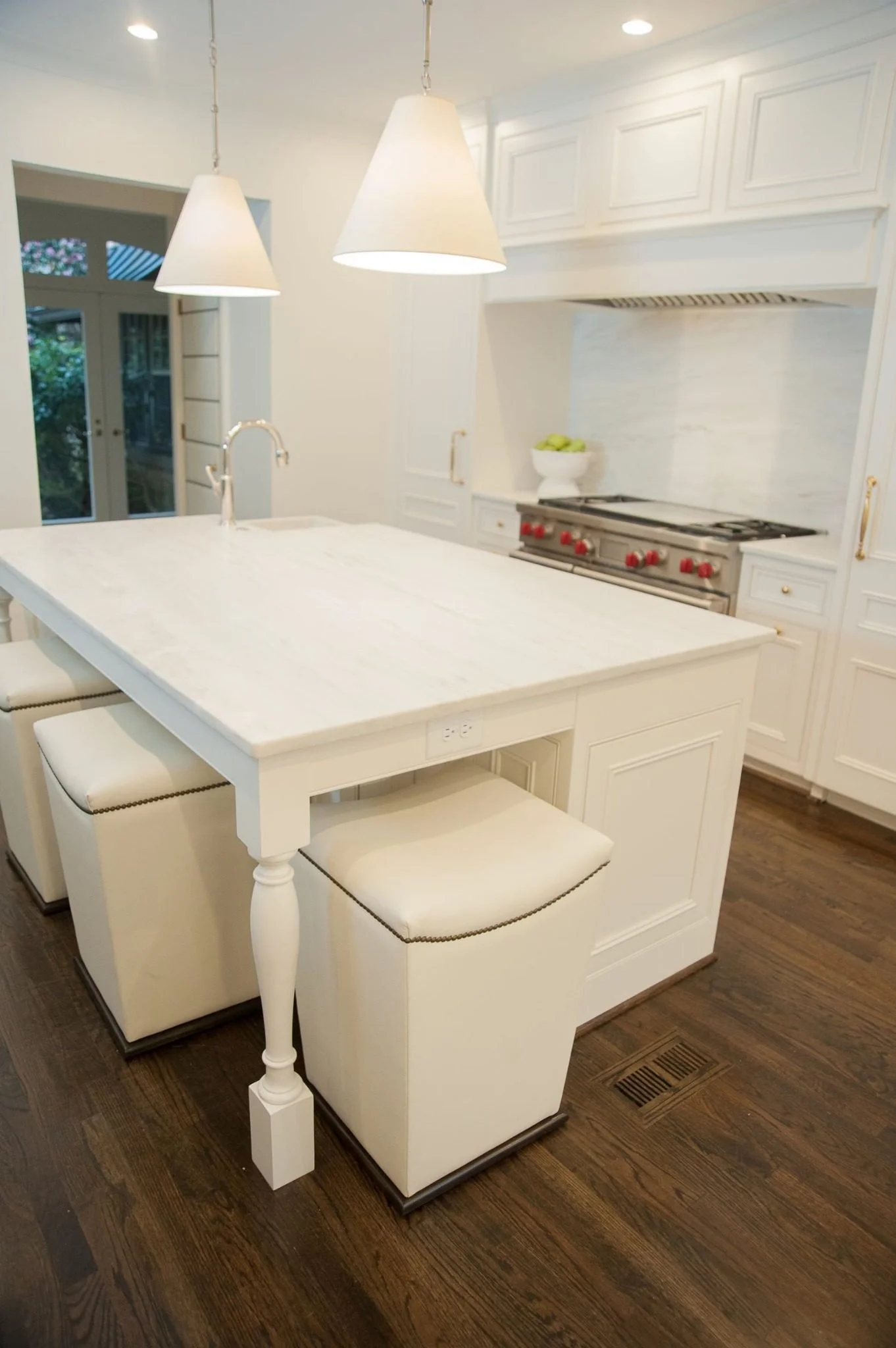 White kitchen island with sink, built-in electrical outlet, upholstered seating and pendant lights