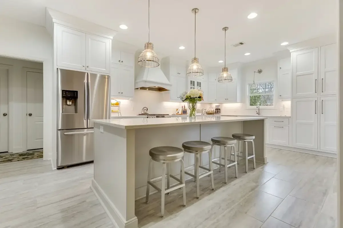 Bright and airy kitchen remodel in Tuscaloosa featuring white custom cabinetry, a large island with quartz countertops, stainless steel appliances, and pendant lighting by Toulmin Kitchen & Bath.