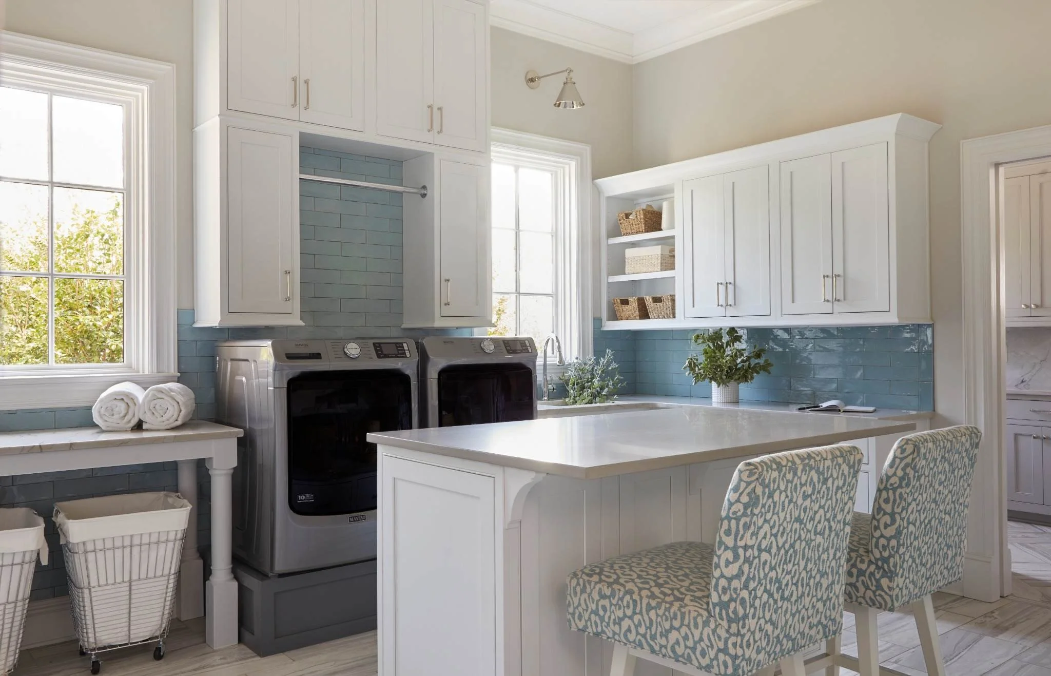 Custom blue laundry room cabinetry with a long white folding counter, hanging rod and built-in storage drawers.